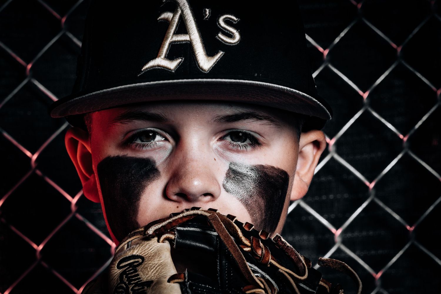 Dramatic sports portrait against chain link fence with dark lighting.