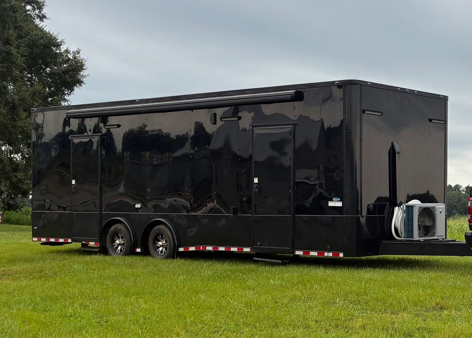 Sleek black enclosed cargo trailer with dual axles parked on green grass under cloudy skies.
