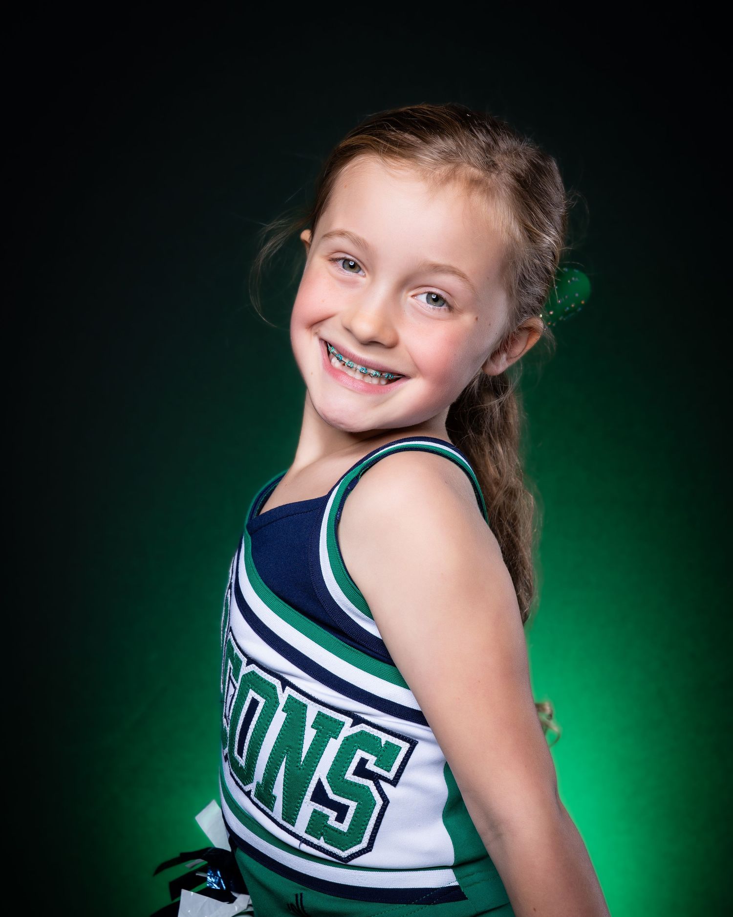 Young cheerleader poses in navy and white uniform against green studio backdrop.