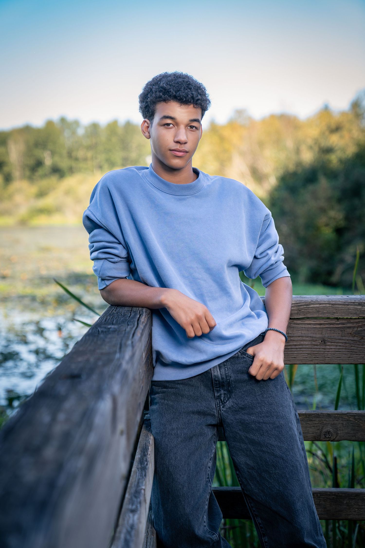 Someone in a blue sweater sits casually on a wooden bench overlooking a scenic landscape.