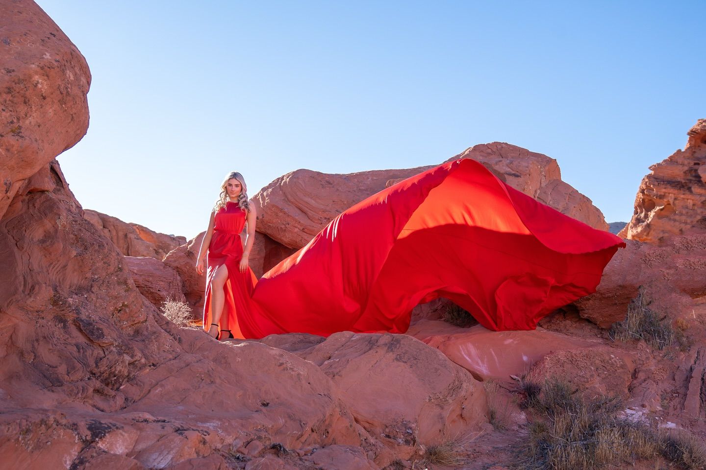 Dramatic red rock formations against bright blue sky in desert landscape at sunset.