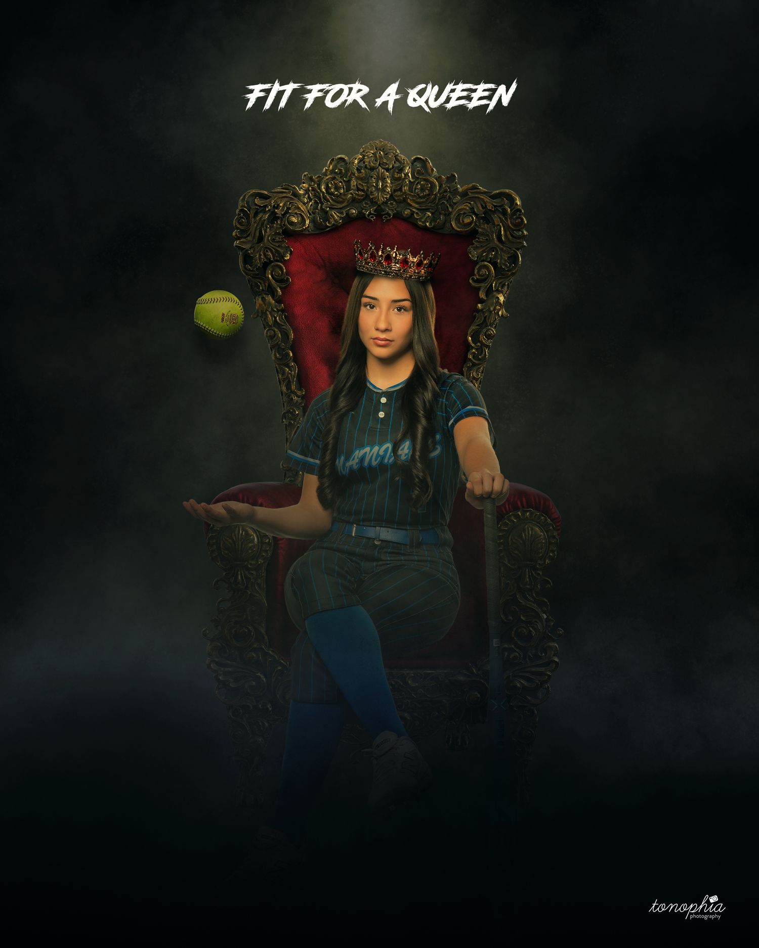 Softball player poses on ornate throne with ball in blue uniform for creative sports portrait.