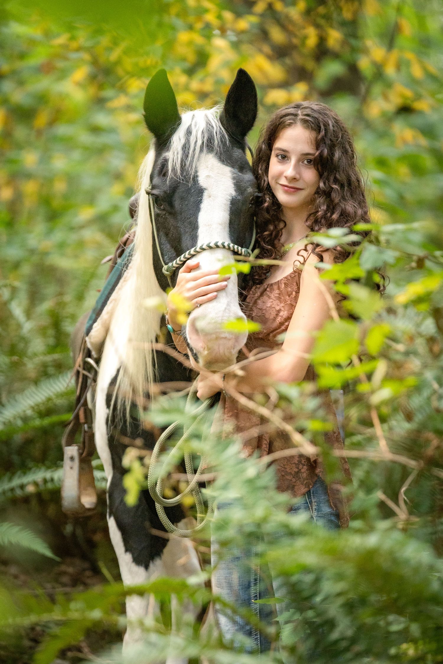 Black and white horse peeks through green foliage in a natural outdoor setting.