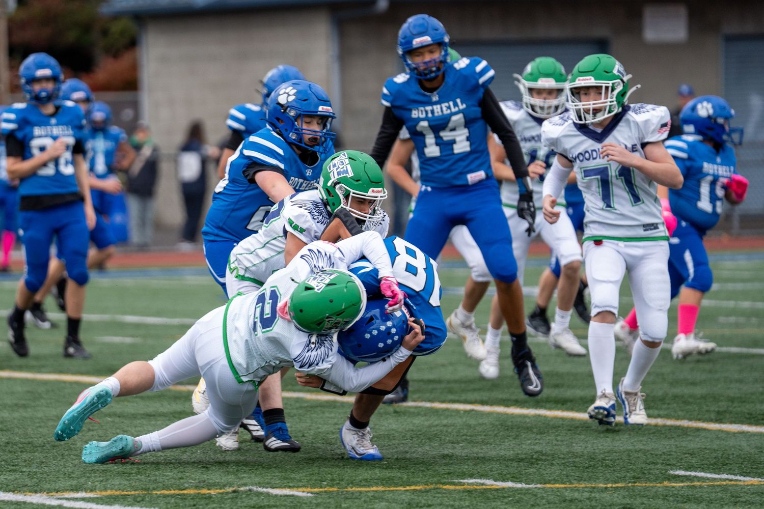 Football players in blue and green uniforms collide during a tackle on the field.