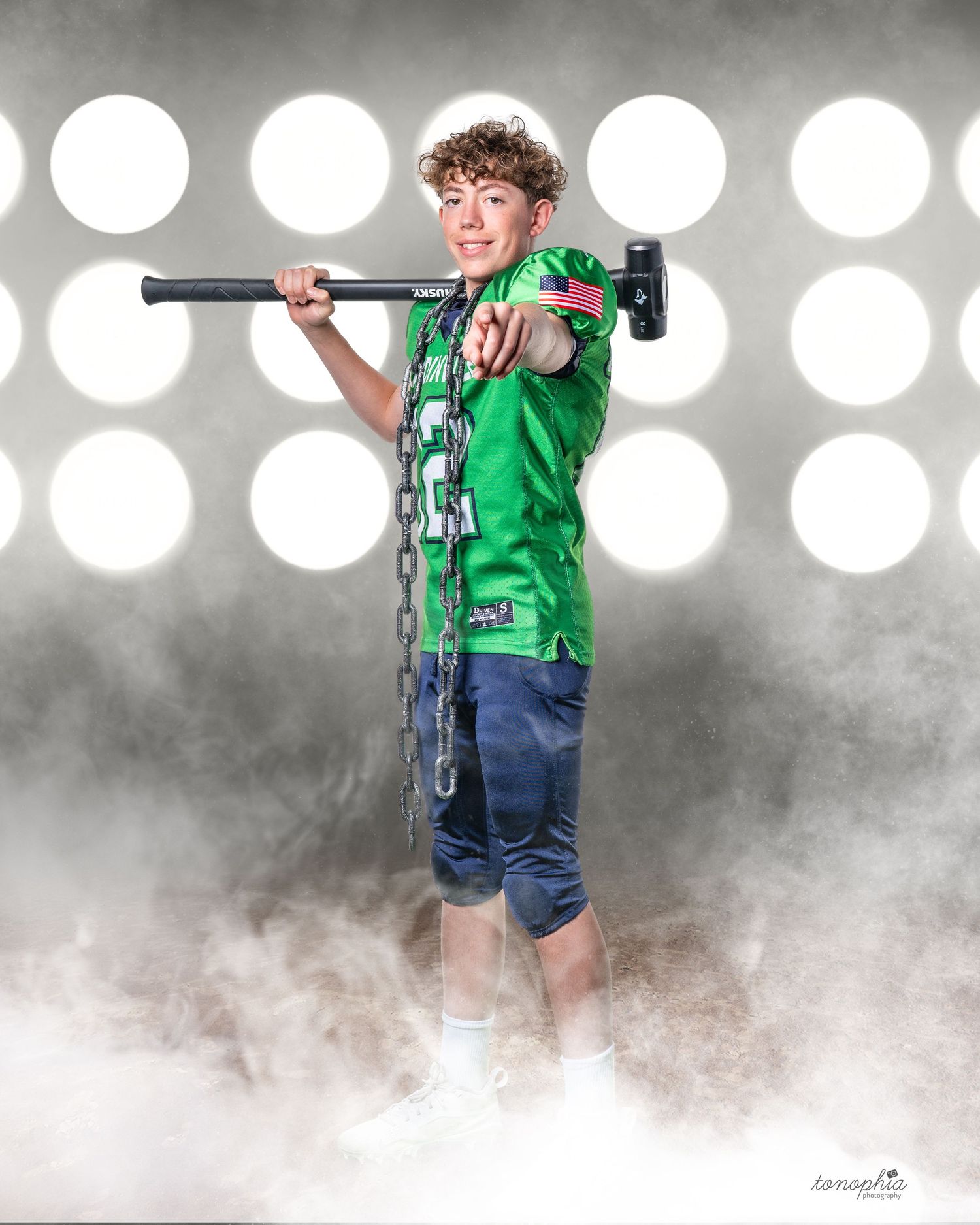 Youth athlete in green jersey poses with football equipment against bright spotlit background.