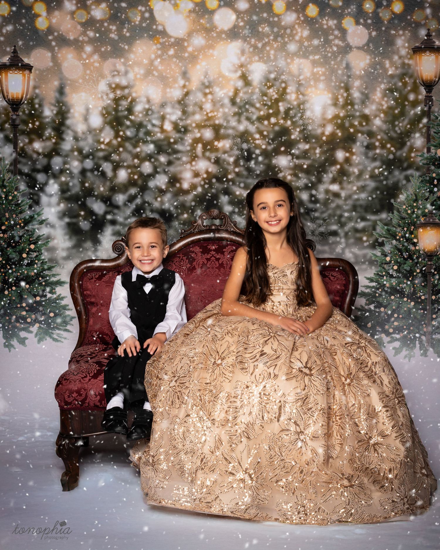 Holiday portrait scene with two children against snowy backdrop with twinkling lights and evergreen garland.