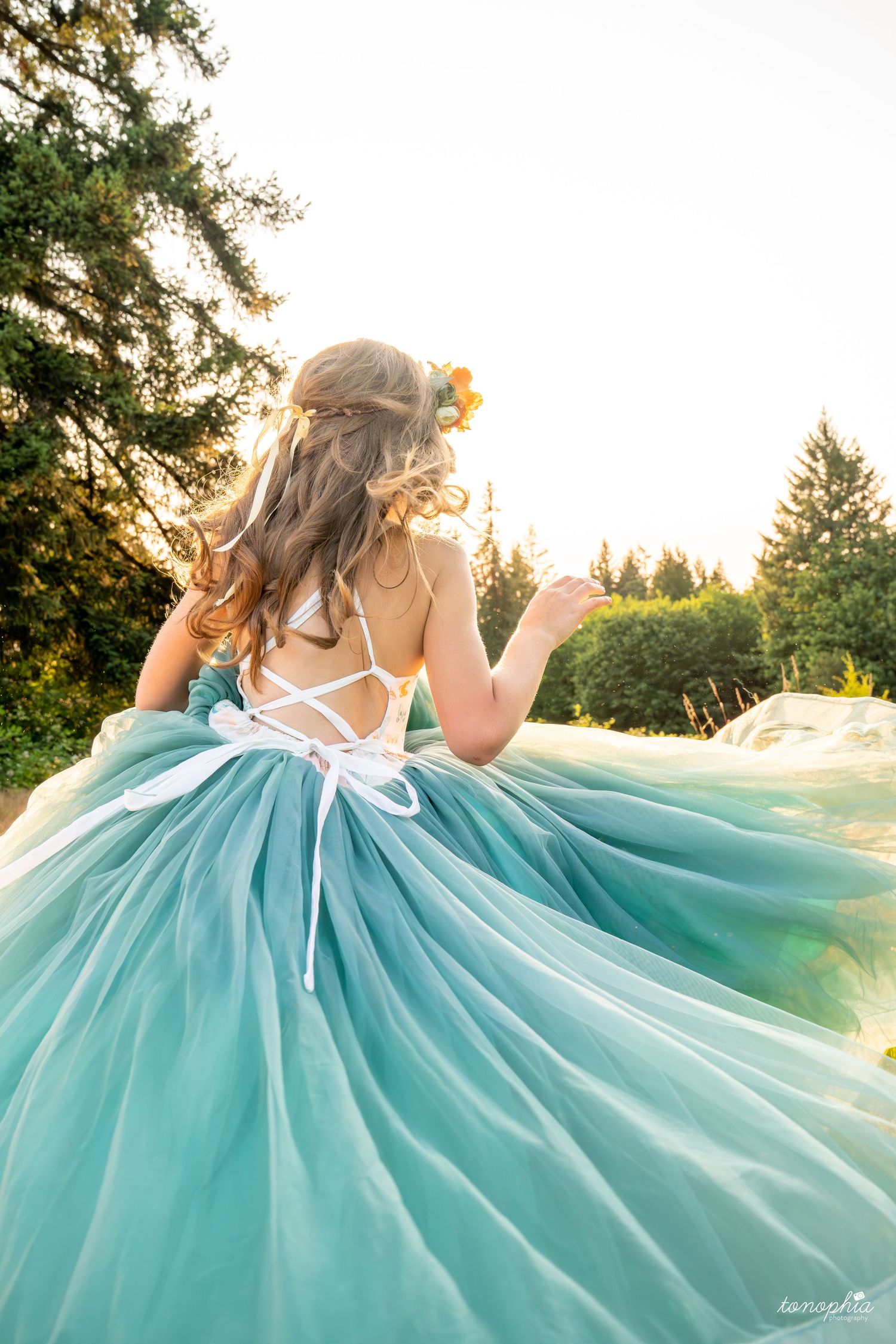 Turquoise ballgown with intricate back detail twirls against white background.
