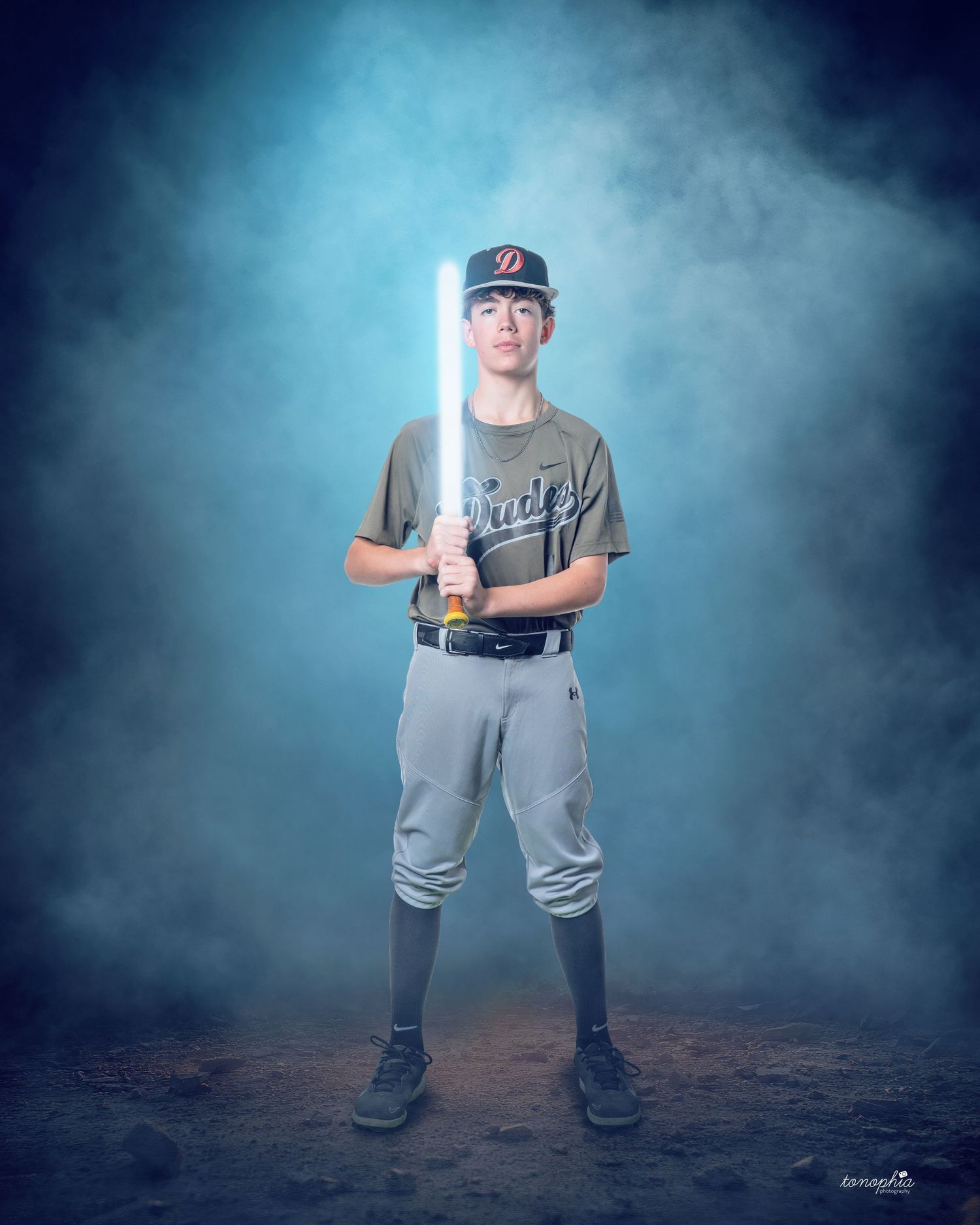 Baseball player in grey uniform stands ready in dramatic pose against misty blue backdrop.