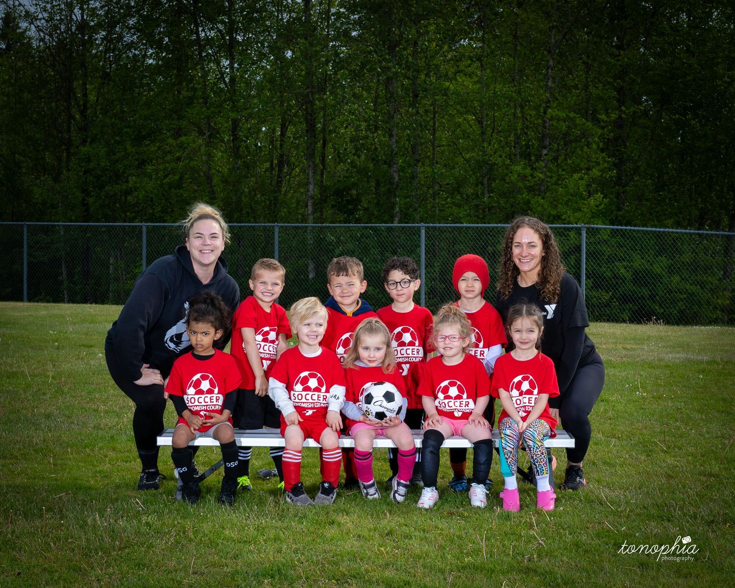 Youth soccer team in red jerseys poses together on grass field for team photo with coaches.