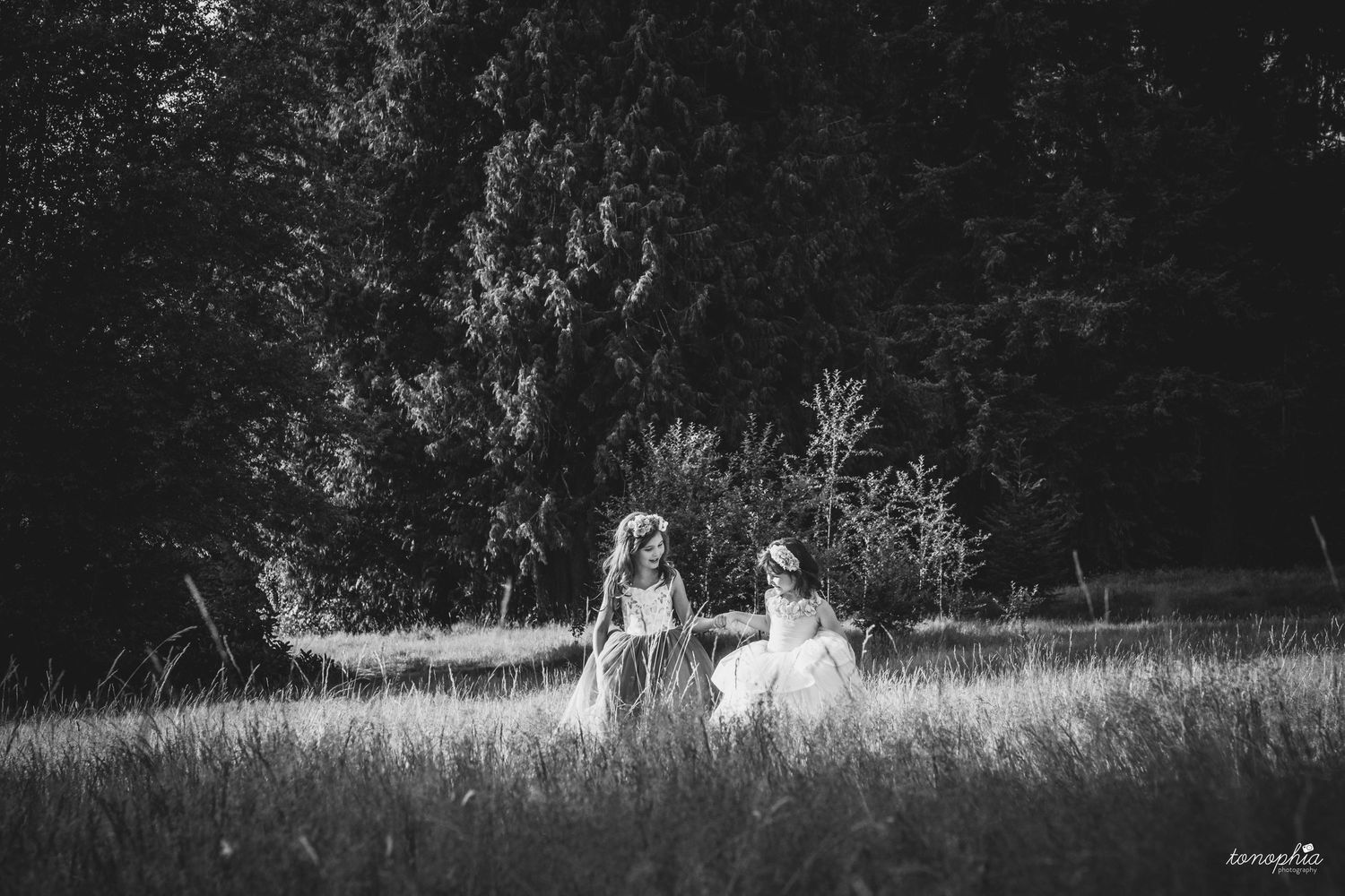 Black and white panoramic view of figures in flowing dresses against a natural landscape.