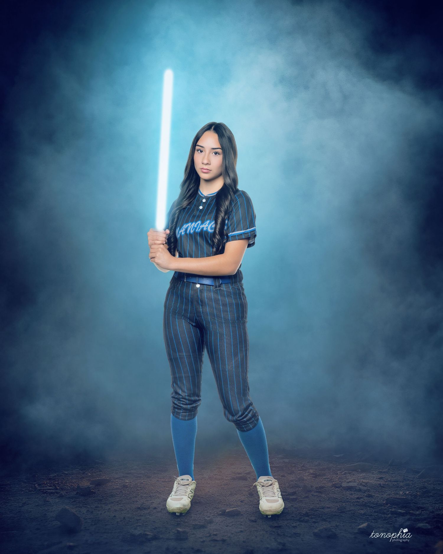 Softball player poses with glowing lightsaber in dramatic blue-lit sports portrait.
