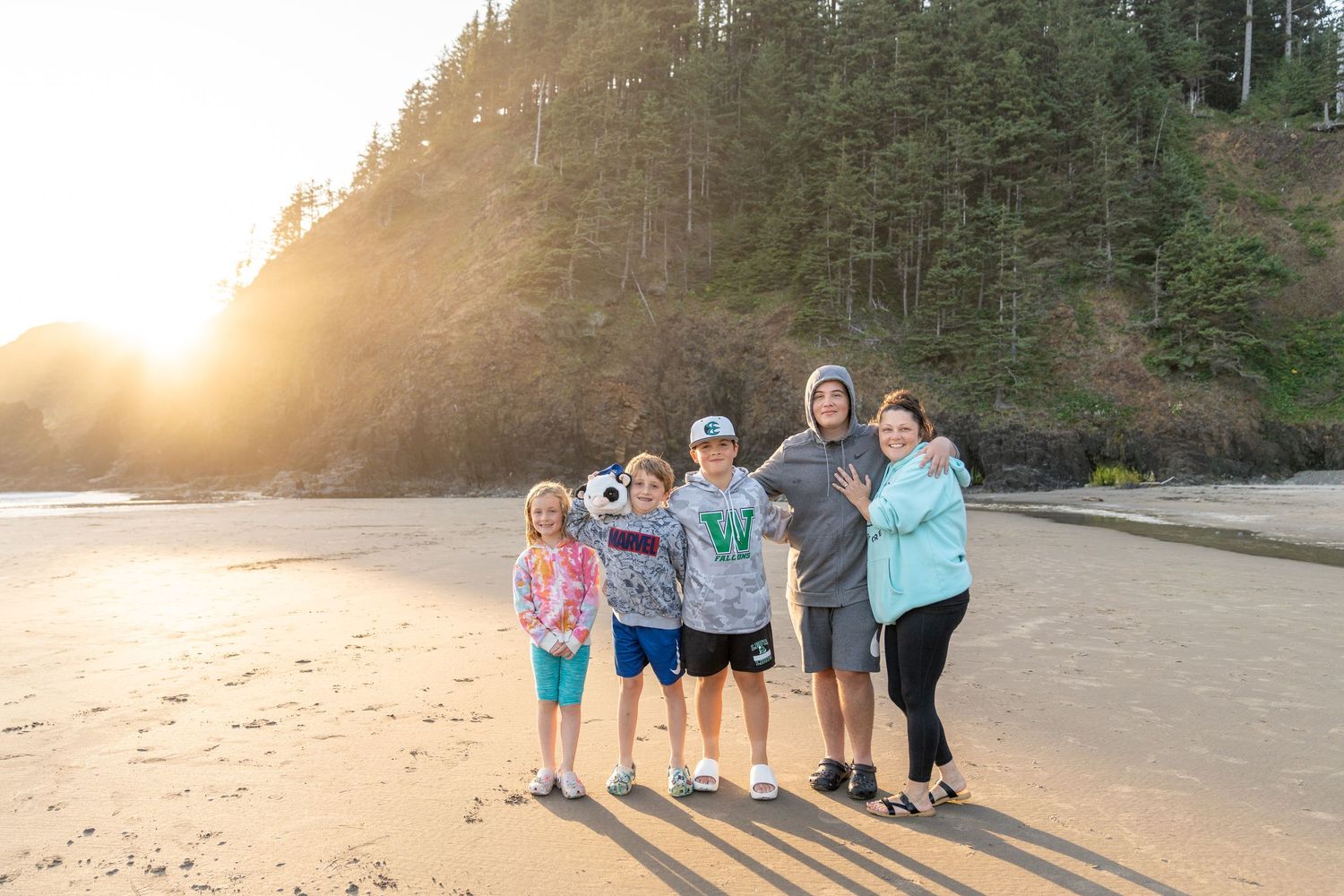 Group standing together on a sandy beach with ocean waves and cliffs during golden hour.