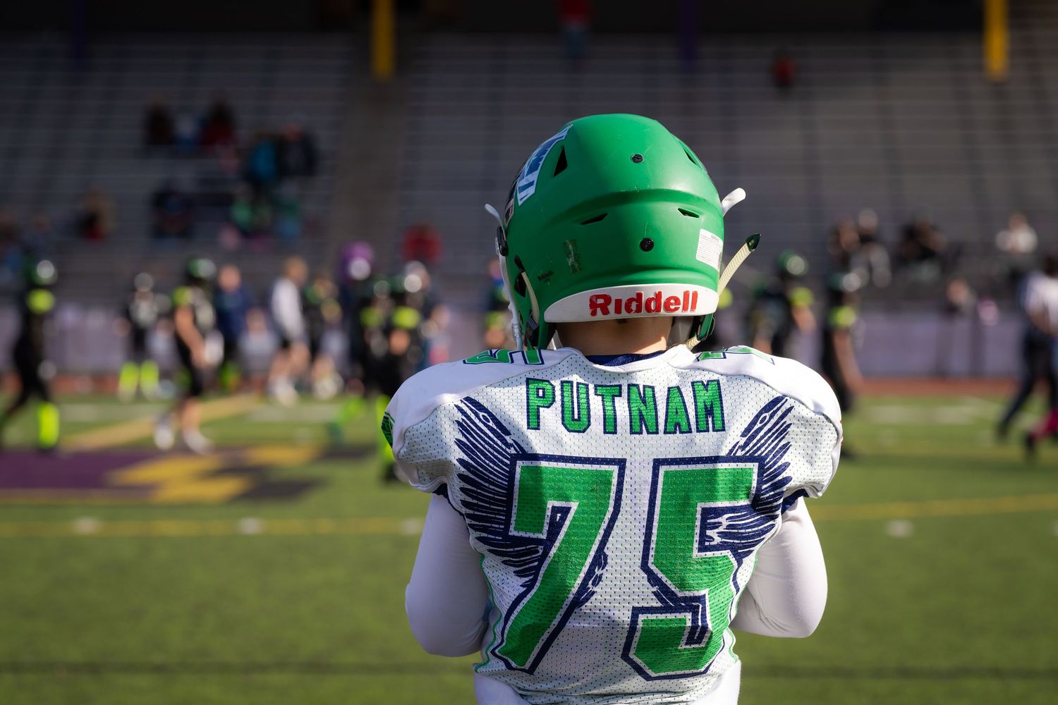 Football players in green helmets and white jerseys on field during game.