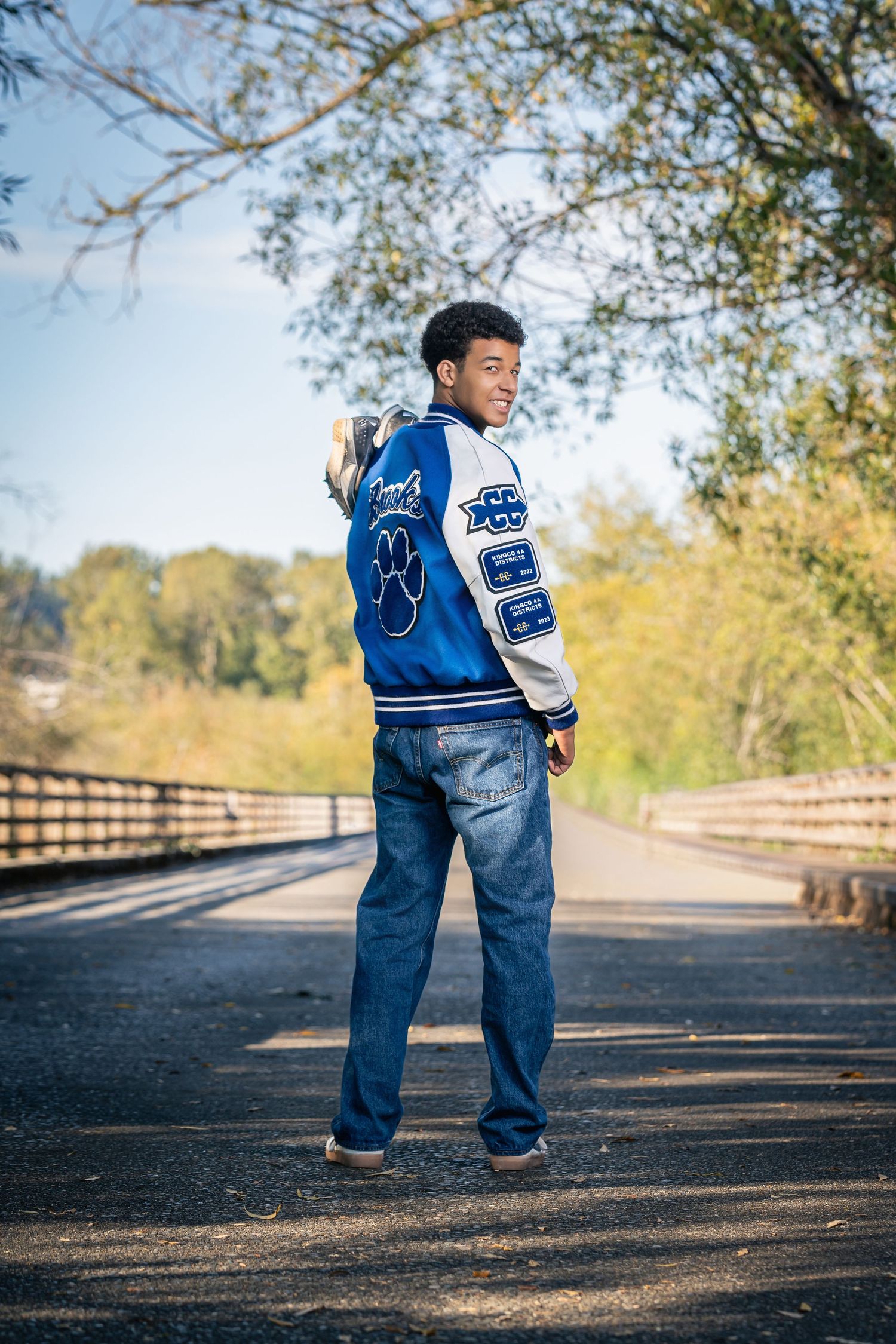 High school senior wearing denim overalls walks along a path on an autumn day.
