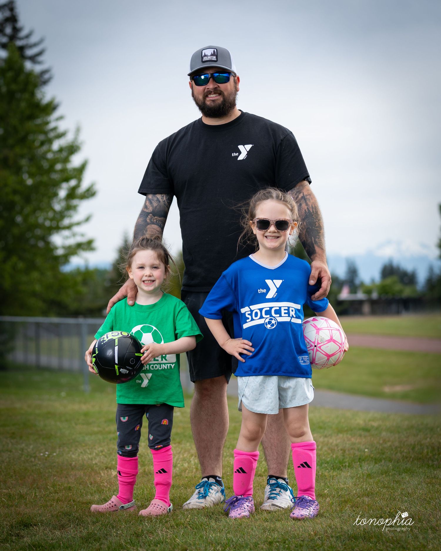 Two children in bright pink socks stand next to an adult on a grassy field with sports equipment.