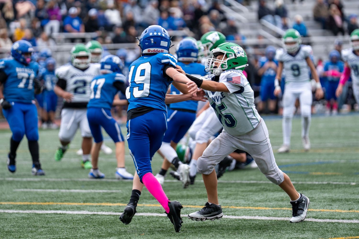 Football players in blue and green jerseys compete during an active play on the field.