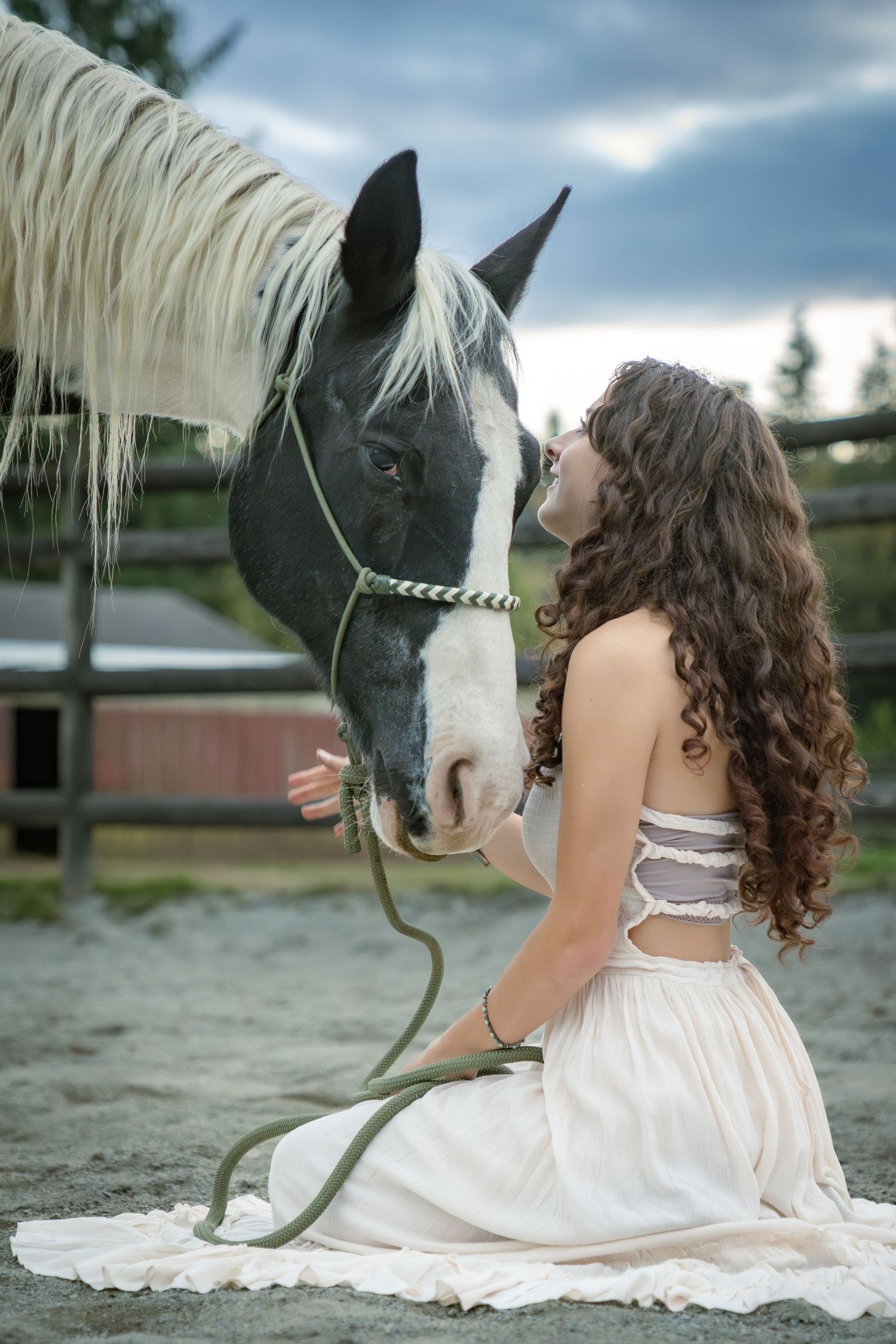 Black and white horse nuzzles close to someone in a flowing white dress.