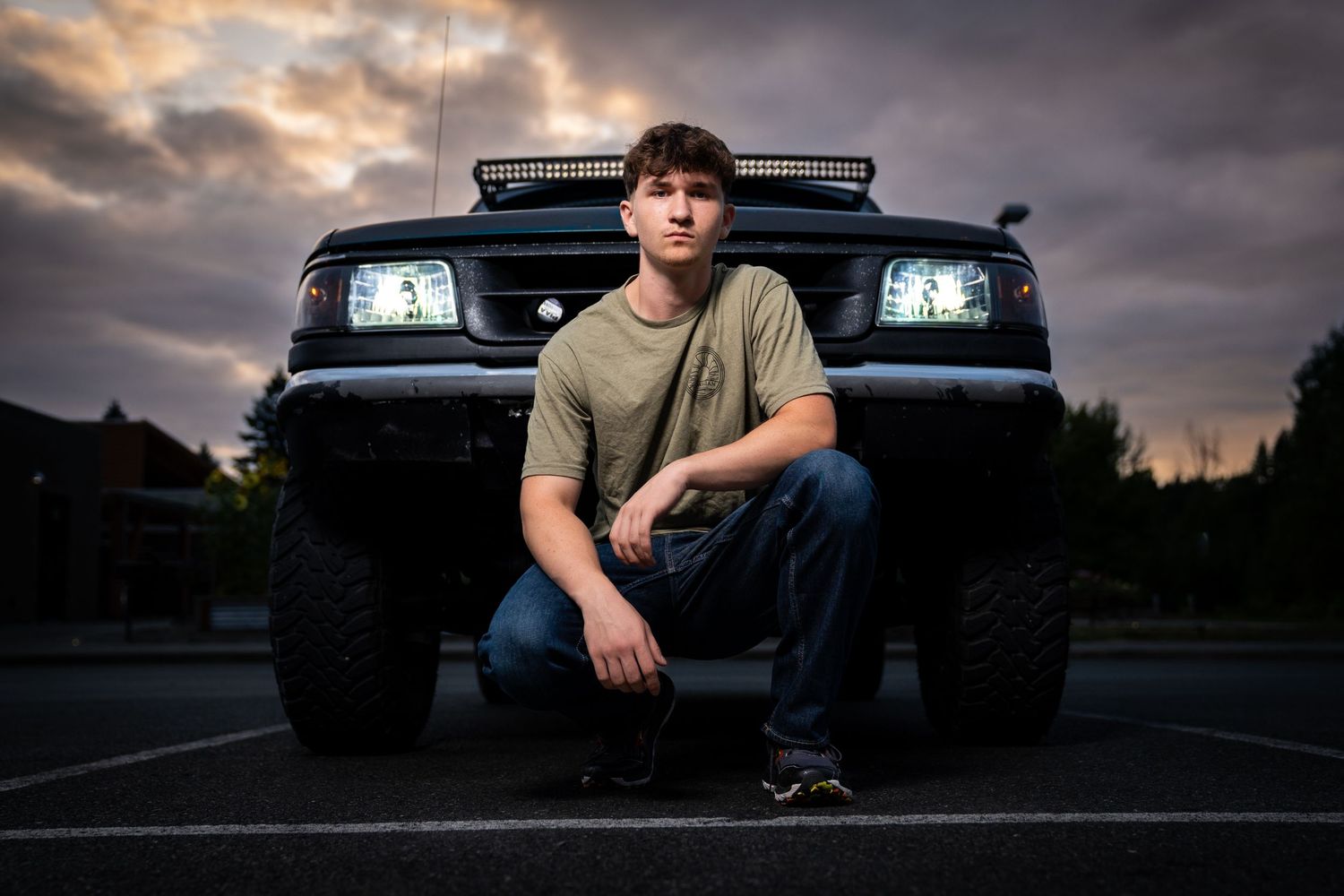 Silhouette poses against dramatic sunset with vehicle headlights.