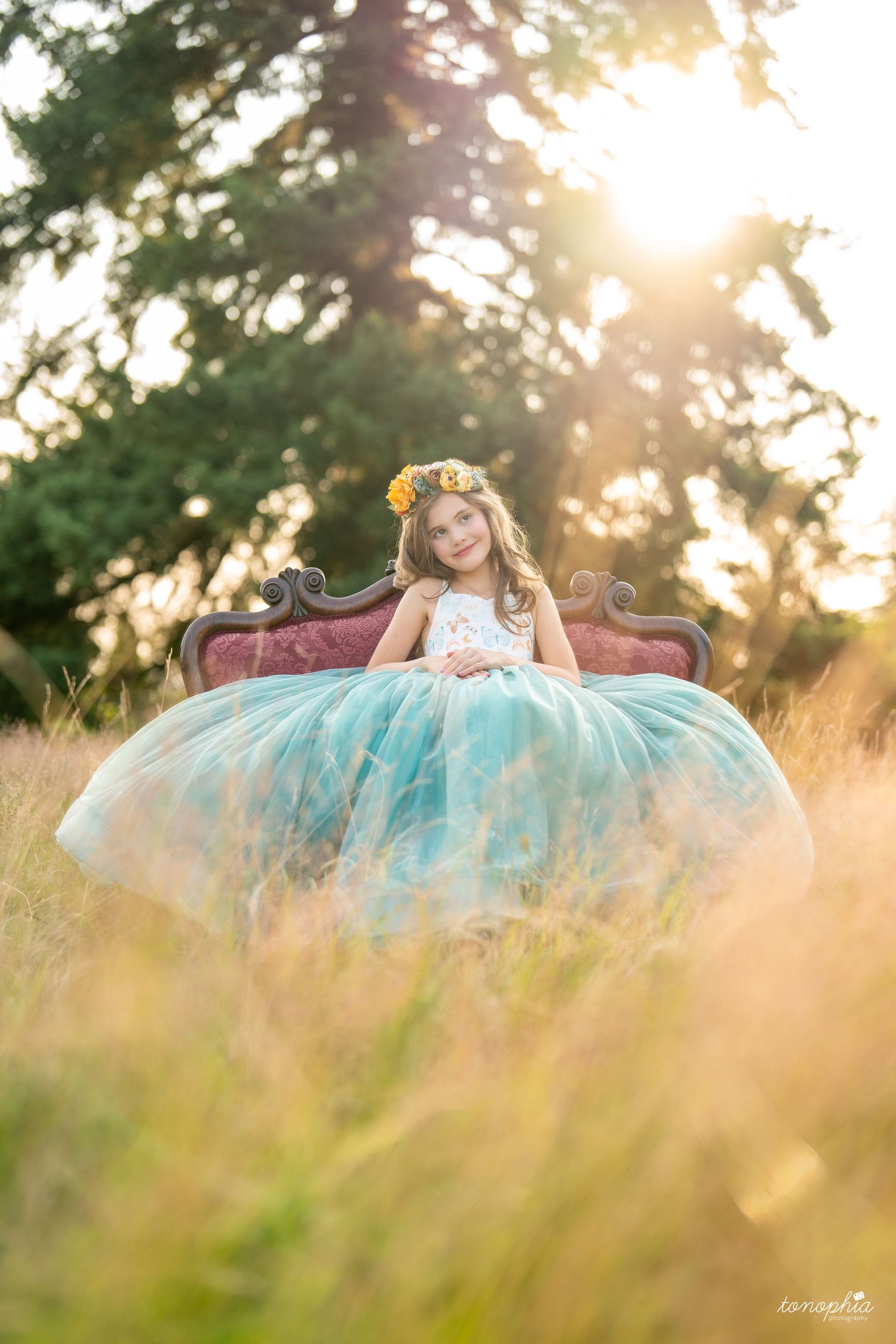 Magical sunset photoshoot with flowing turquoise gown spread across golden grass.
