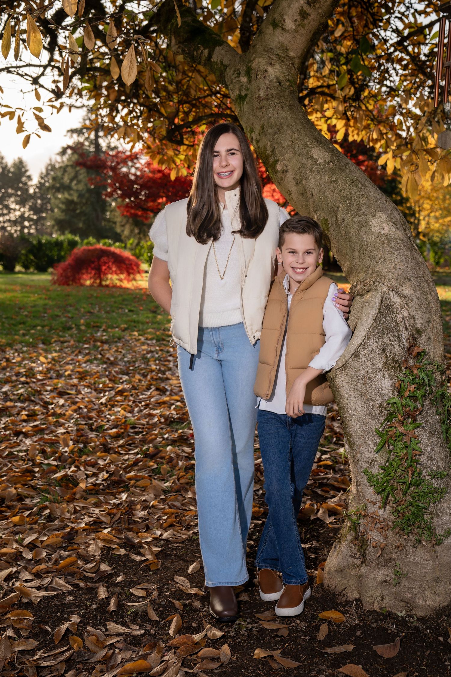 Casual autumn photoshoot under a large tree with golden leaves scattered on the ground.