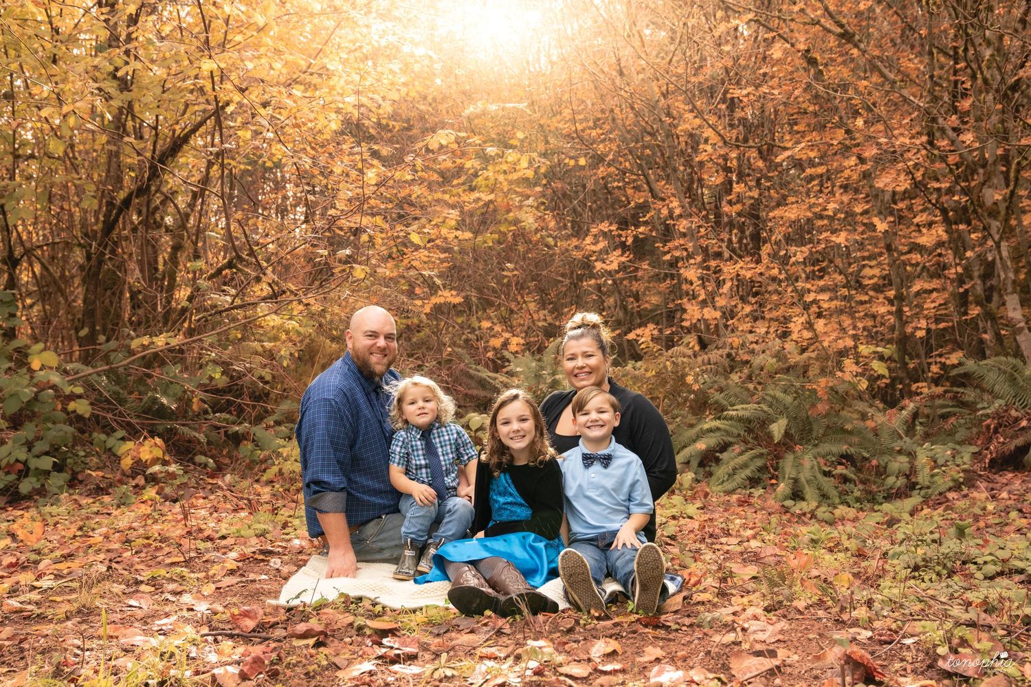 Family gathering for photos in a sun-drenched autumn setting with fallen leaves.