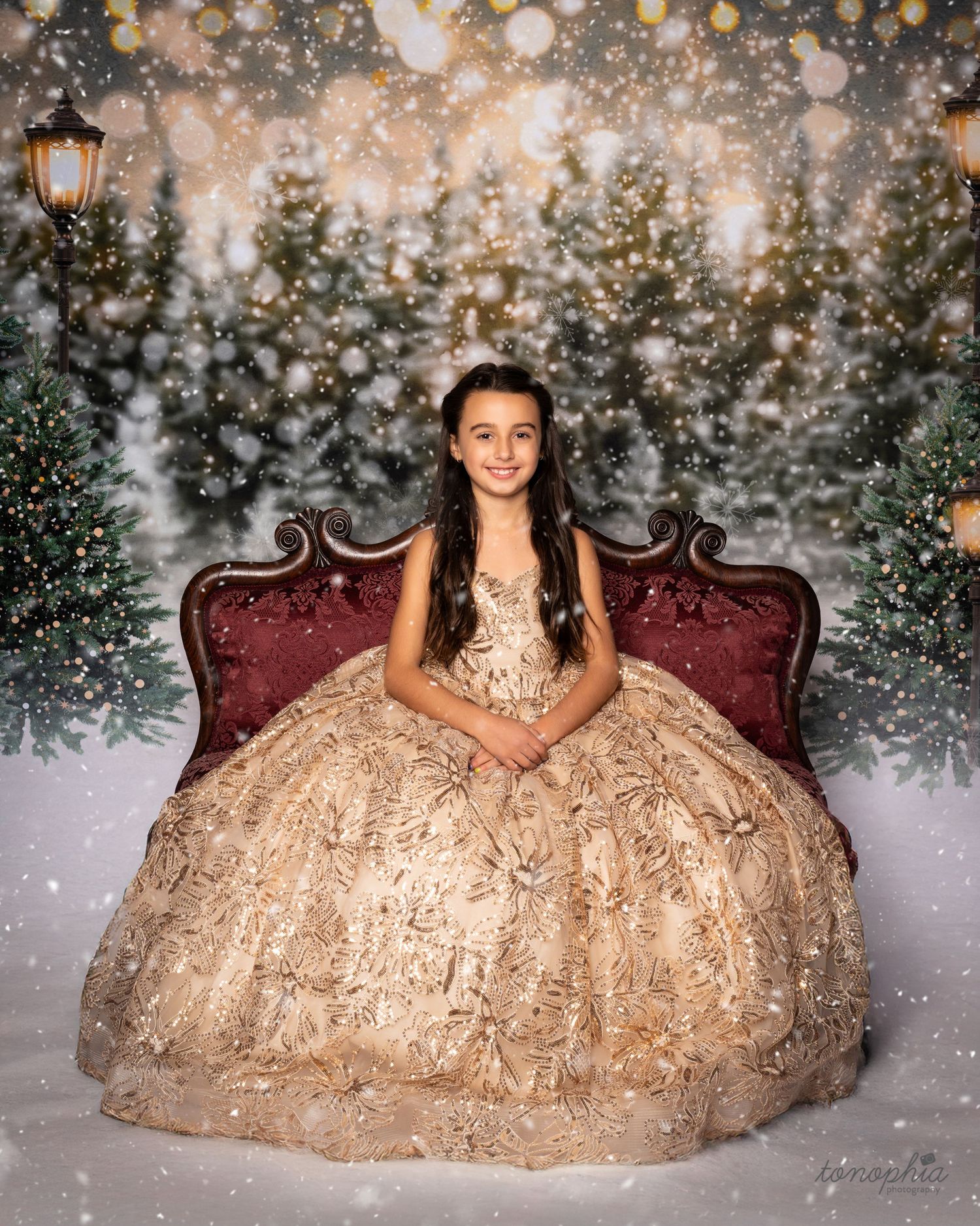 Elegant gold sequined gown photographed in winter wonderland setting with bokeh lights and evergreen decor.
