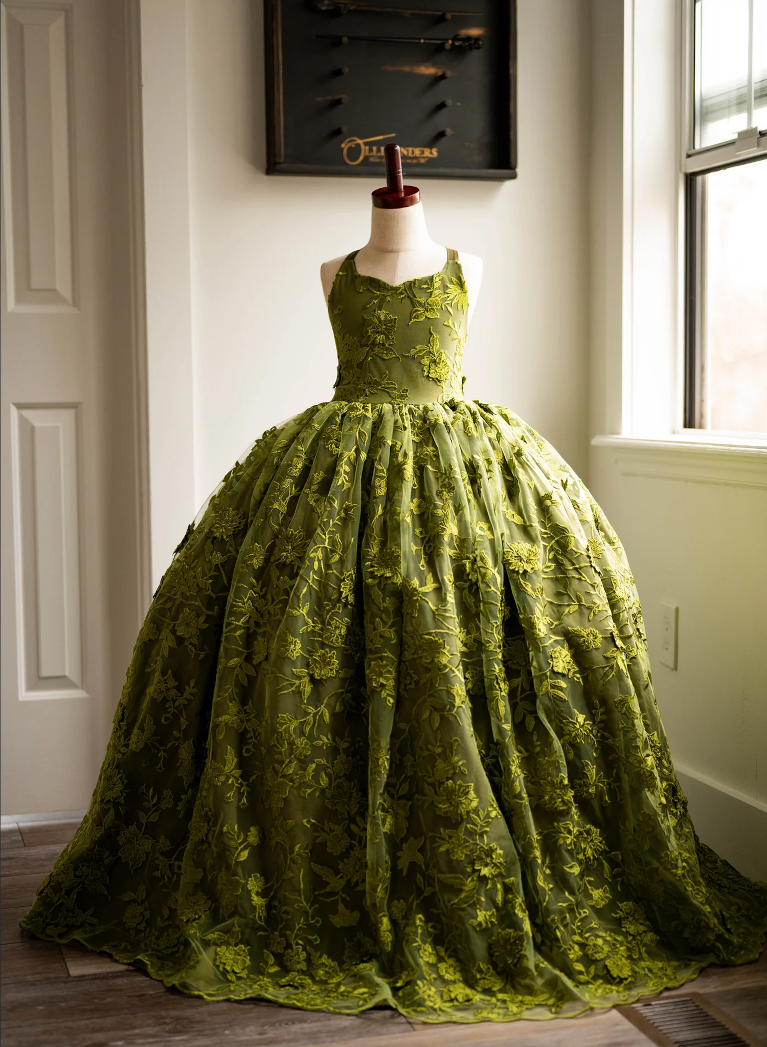 Dramatic moss green ballgown with textured fabric displayed on mannequin in sunlit room.
