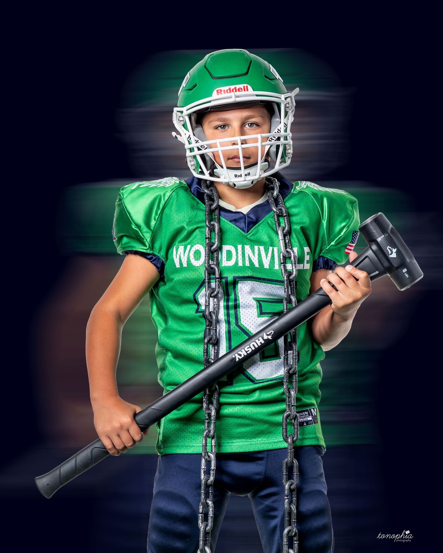 Youth athlete in green Woodinville uniform holds football equipment in dramatic lighting.