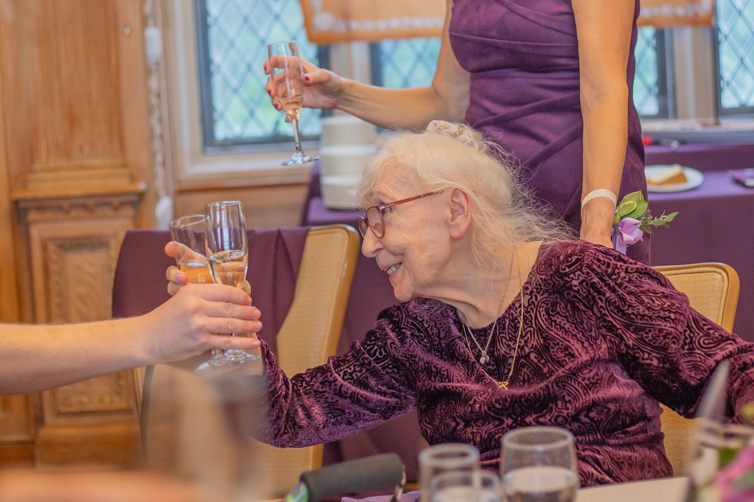 A person in a burgundy velvet top raises a champagne glass in a toast at an elegant dining table.