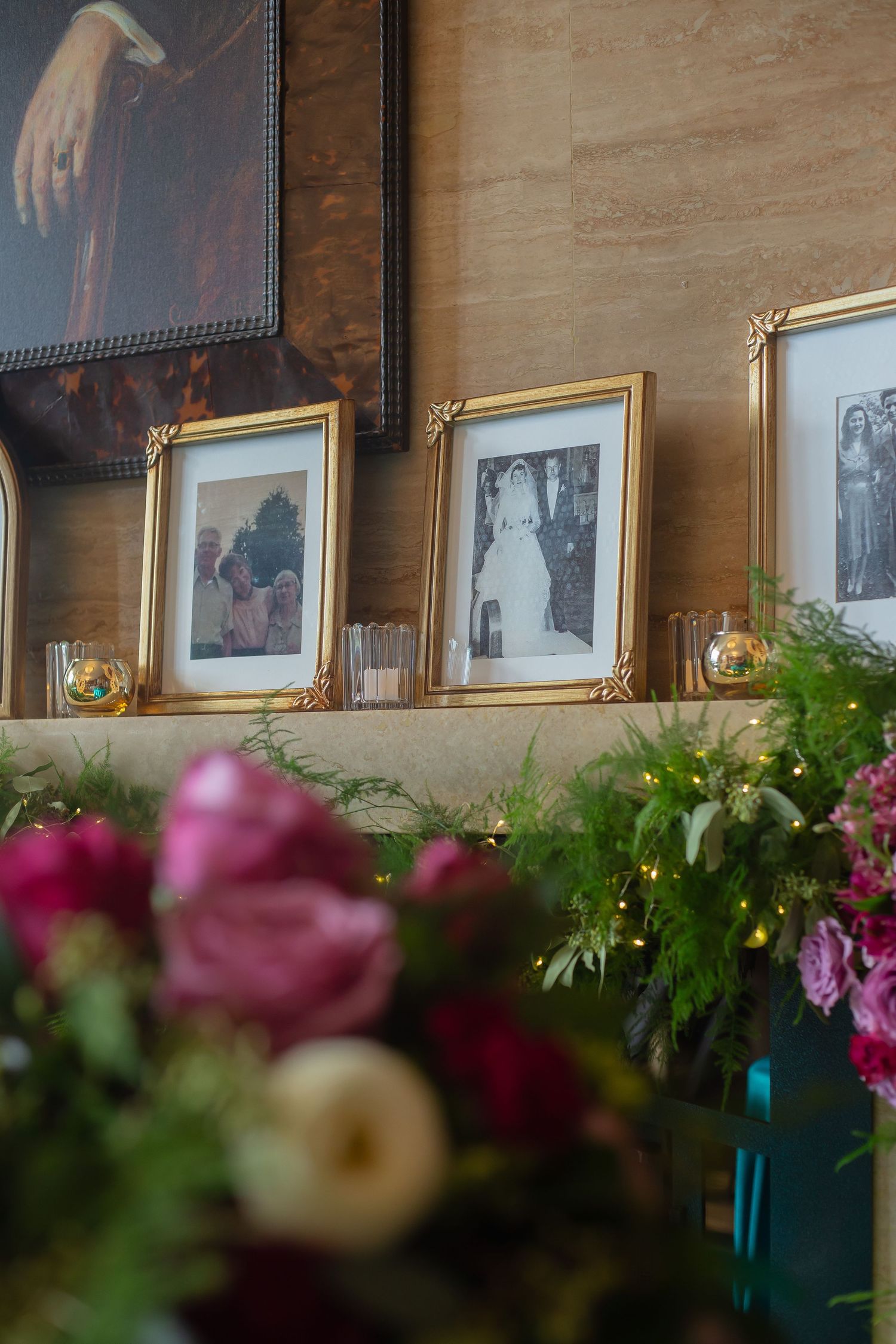 A row of framed photographs hangs on a wooden wall with pink flowers and greenery in the foreground.