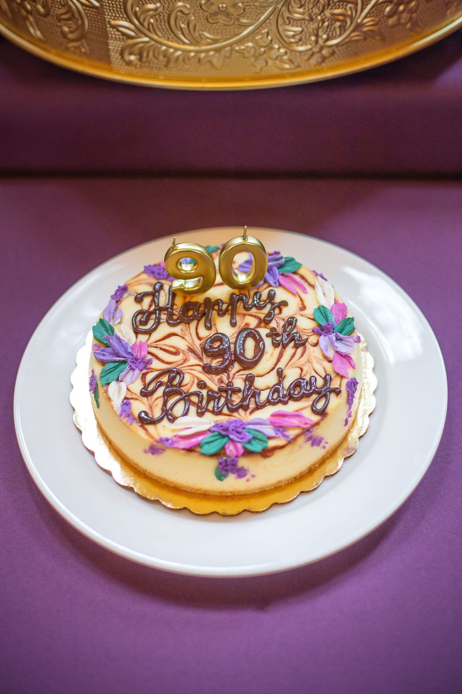 A round birthday cake decorated with colorful flowers and a gold '30' topper sits on a white plate against a purple background.