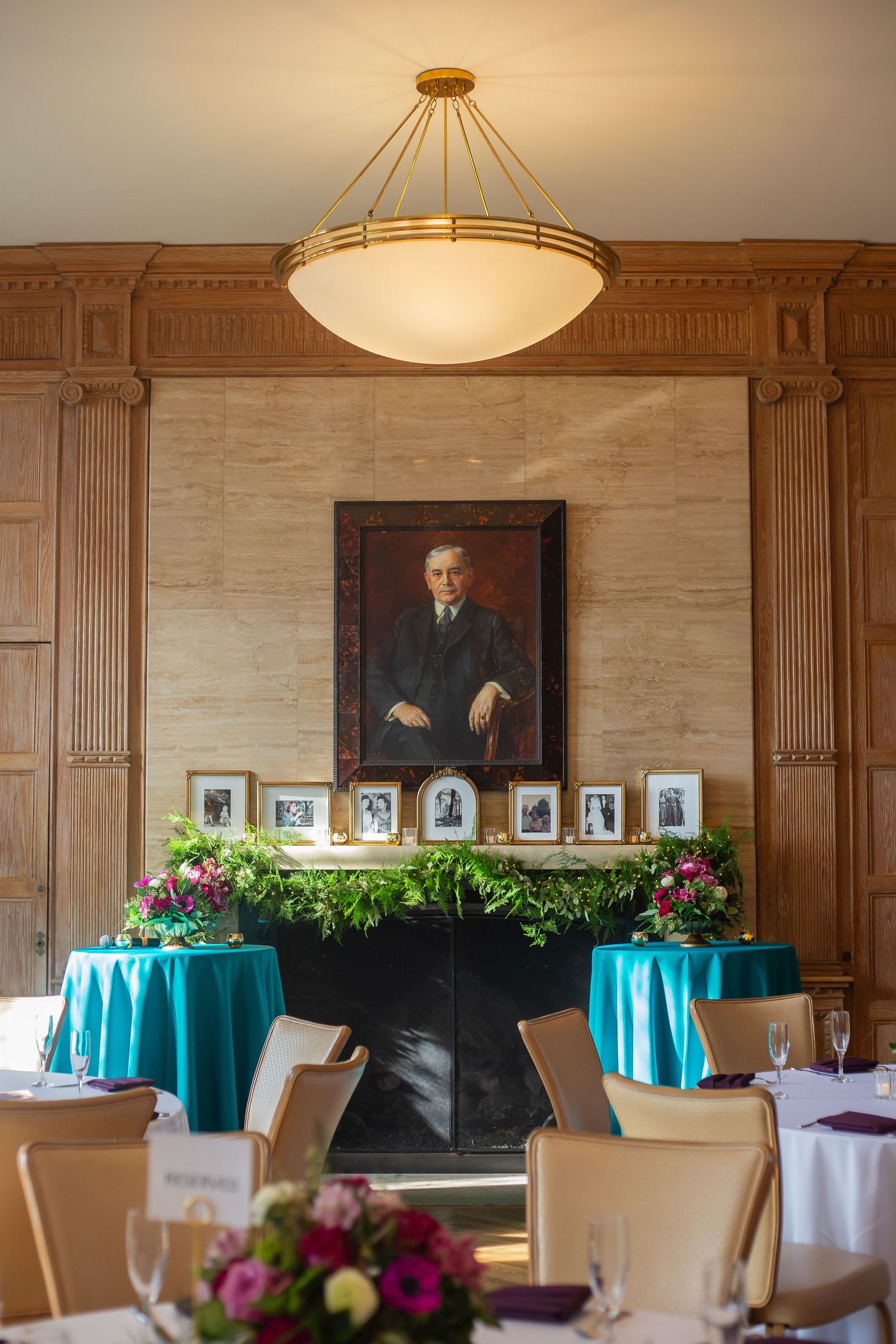Elegant banquet room with wooden panels, cream walls, teal tablecloths, and floral centerpieces under pendant lighting.