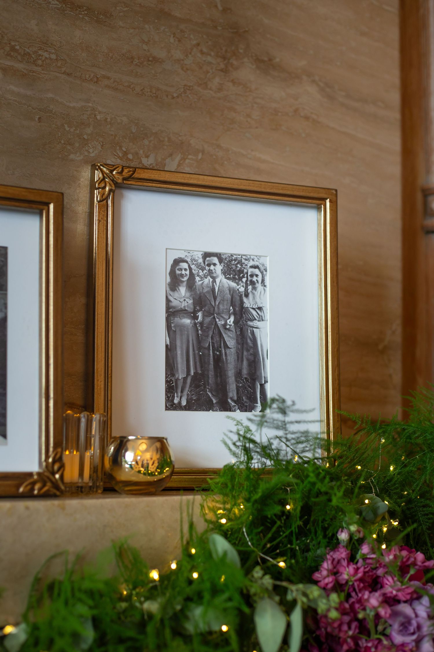 Vintage black and white photographs in gold frames displayed on wall above green plants with purple flowers.