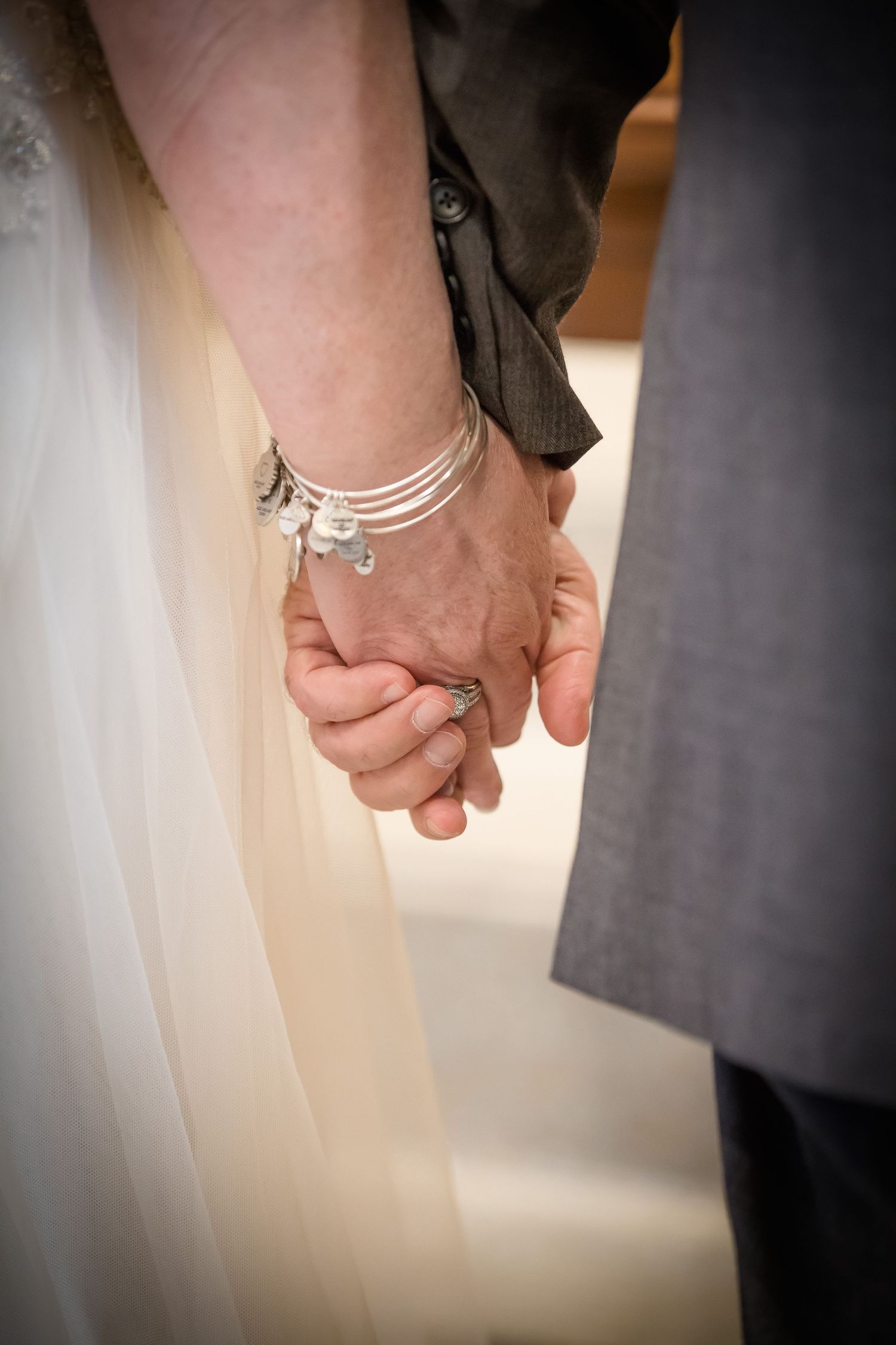 Bride and groom holding hands at wedding ceremony, bride wearing silver charm bracelet and engagement ring.