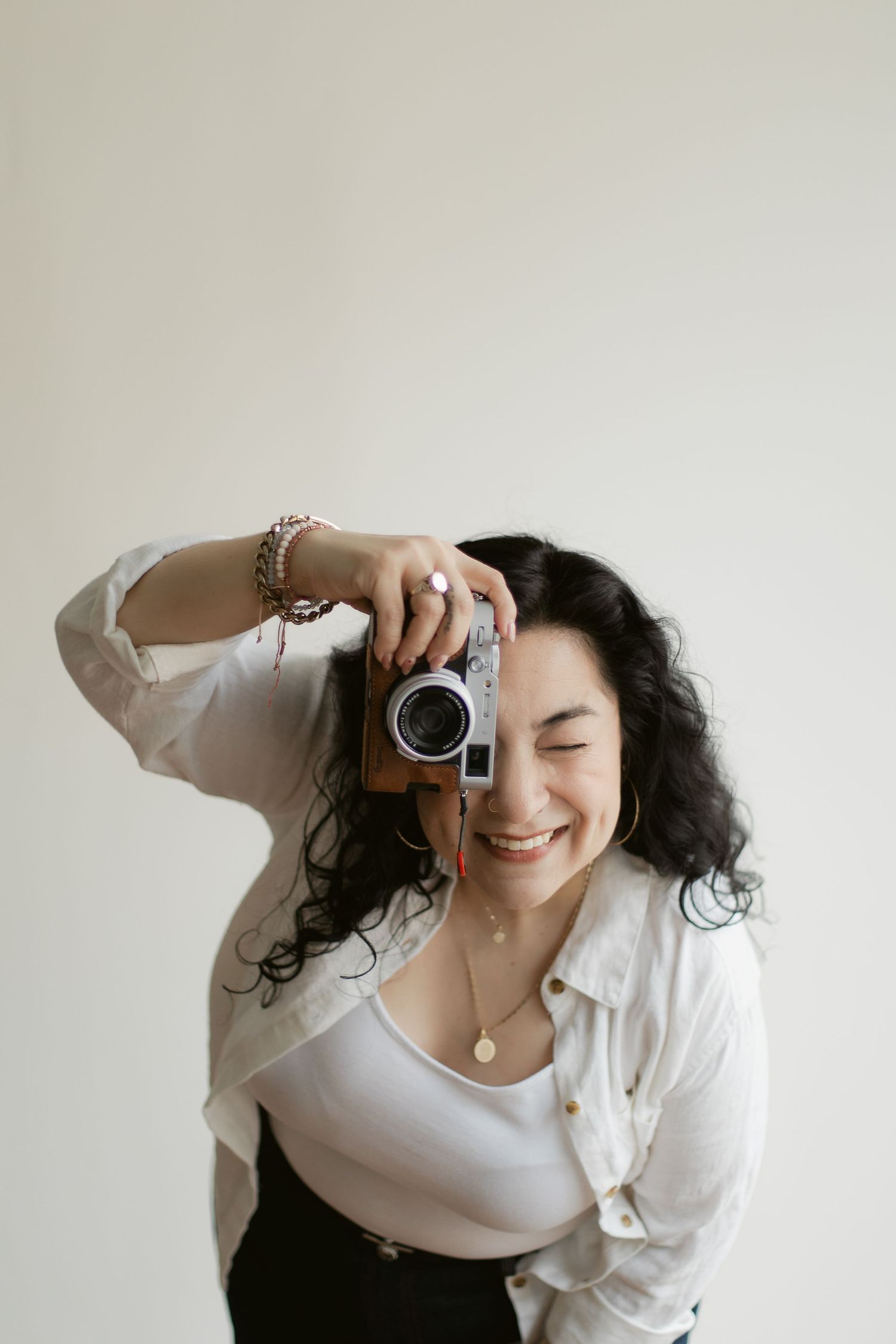 A photographer in white clothing holds a vintage camera while taking photos against a light background.