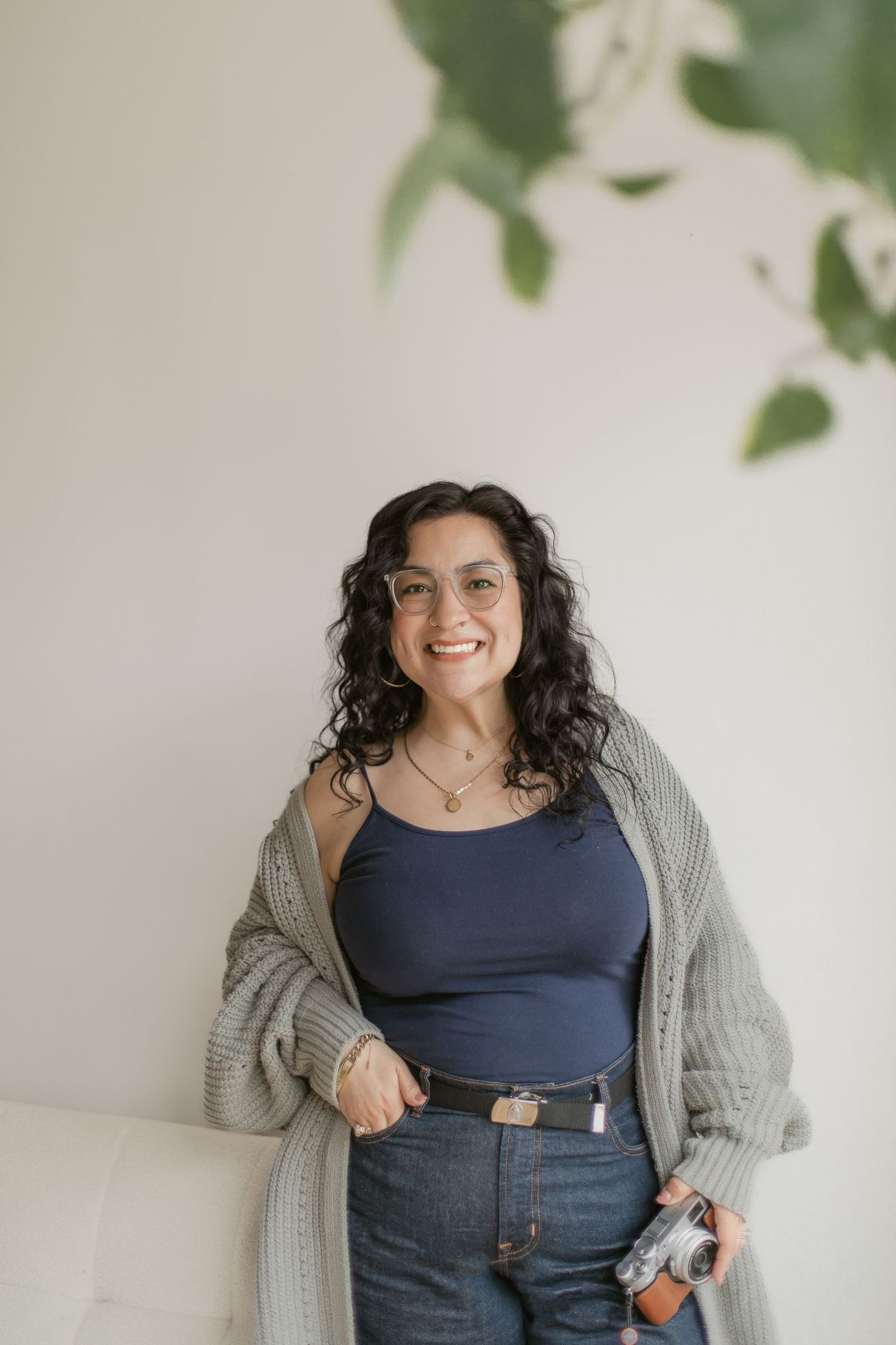 A series of four casual lifestyle photos showing someone in a navy top and gray cardigan against a white wall with plants.