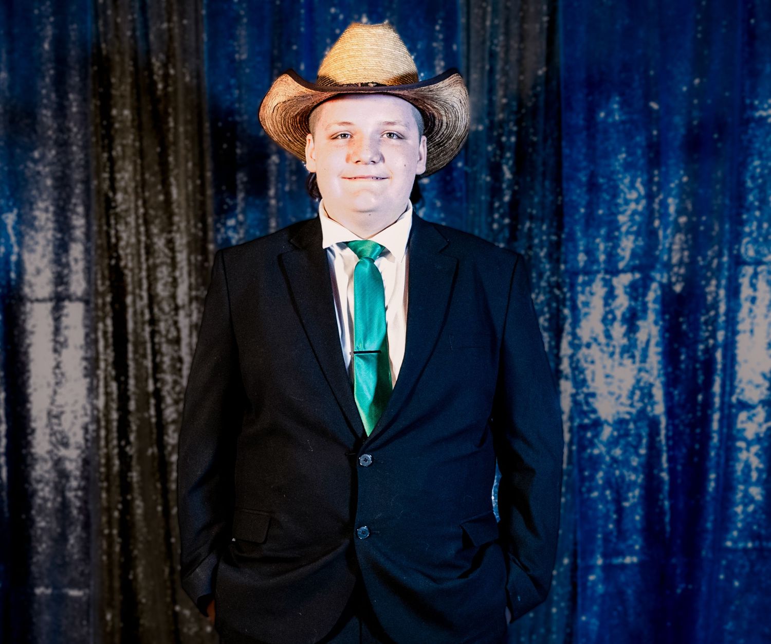 Professional portrait against blue textured backdrop with person wearing black suit and emerald green tie.