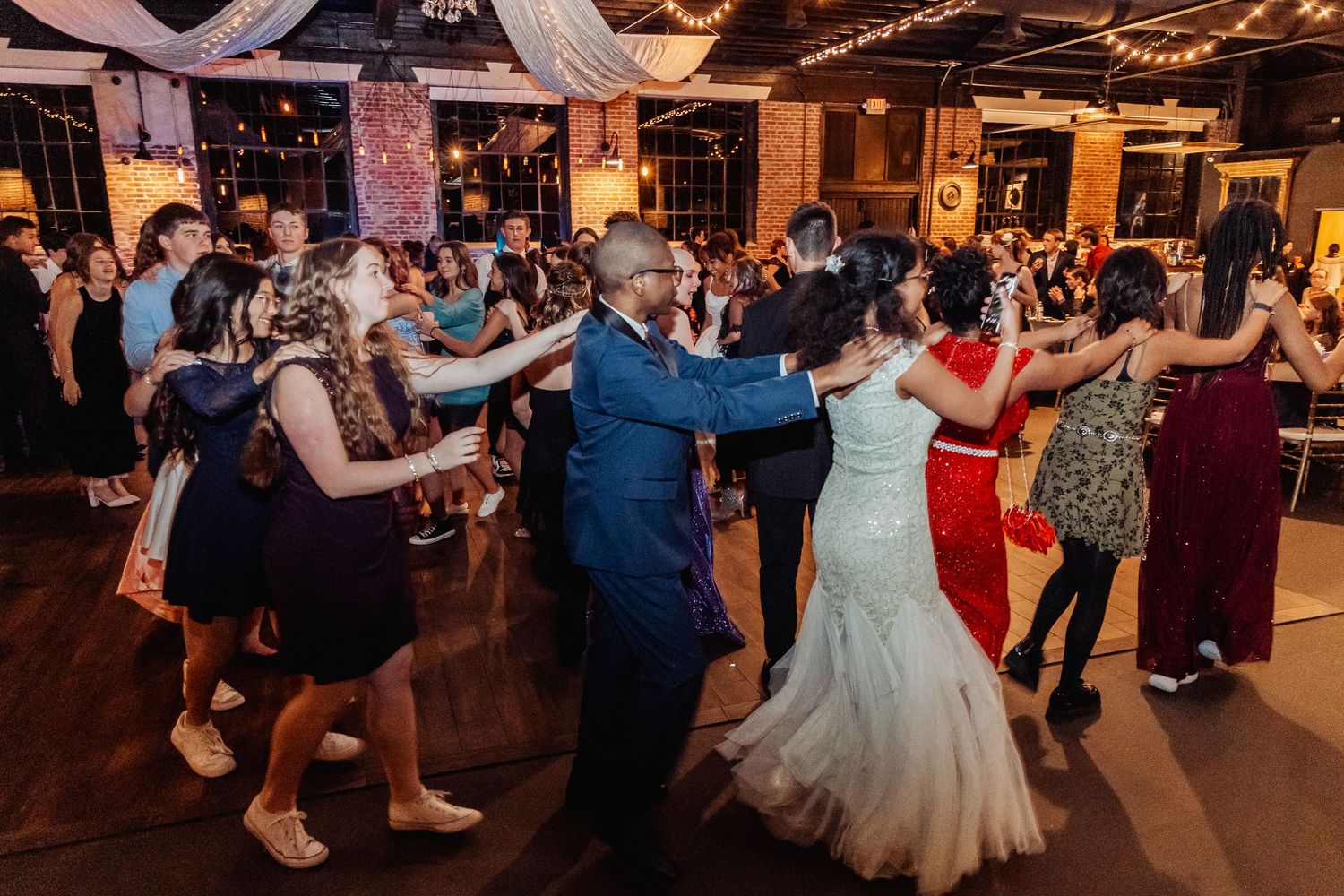 Wedding guests dance together on a dimly lit reception dance floor during an evening celebration.