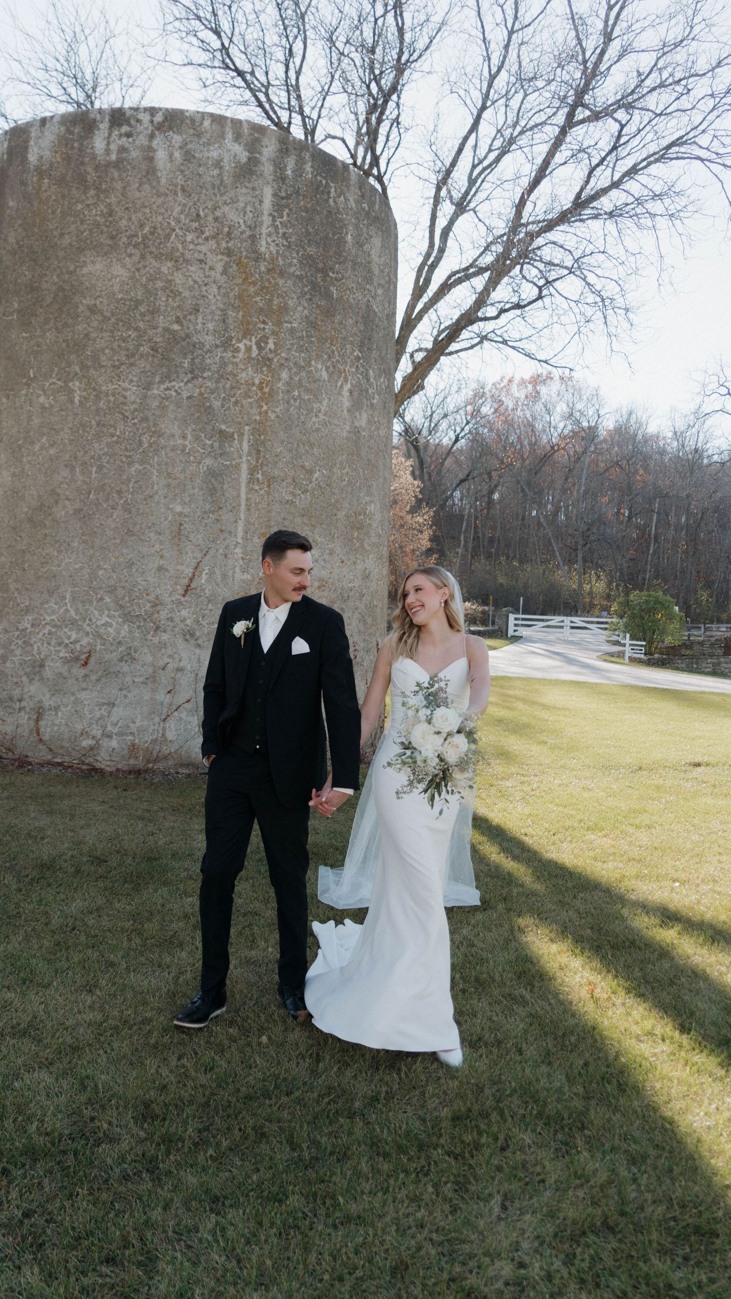 A bride and groom share a joyful moment together on their wedding day in front of a stone wall on a sunny winter afternoon.