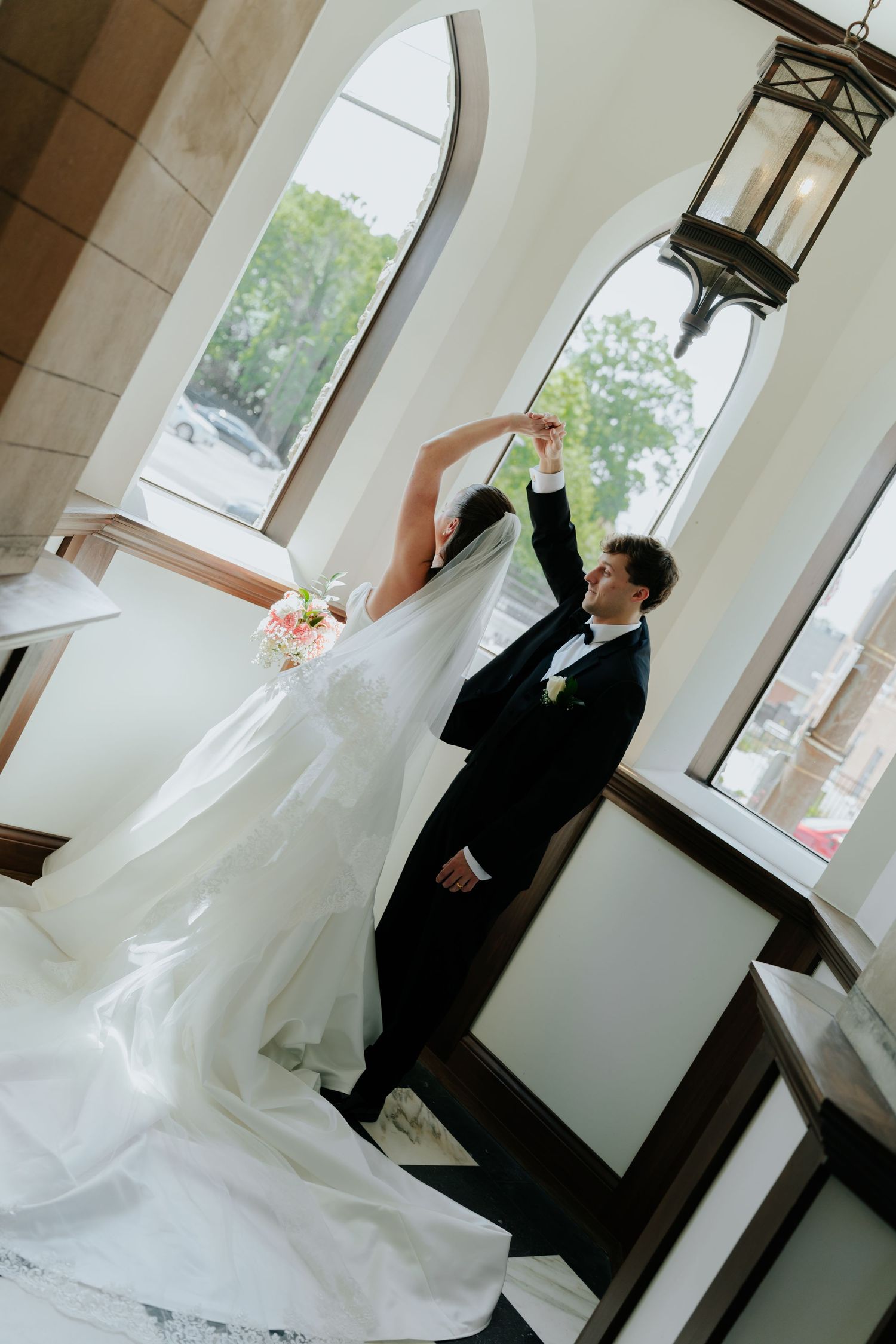 Bride and groom dancing elegantly in a sunlit church, bride in flowing white gown with veil, groom in black tuxedo.