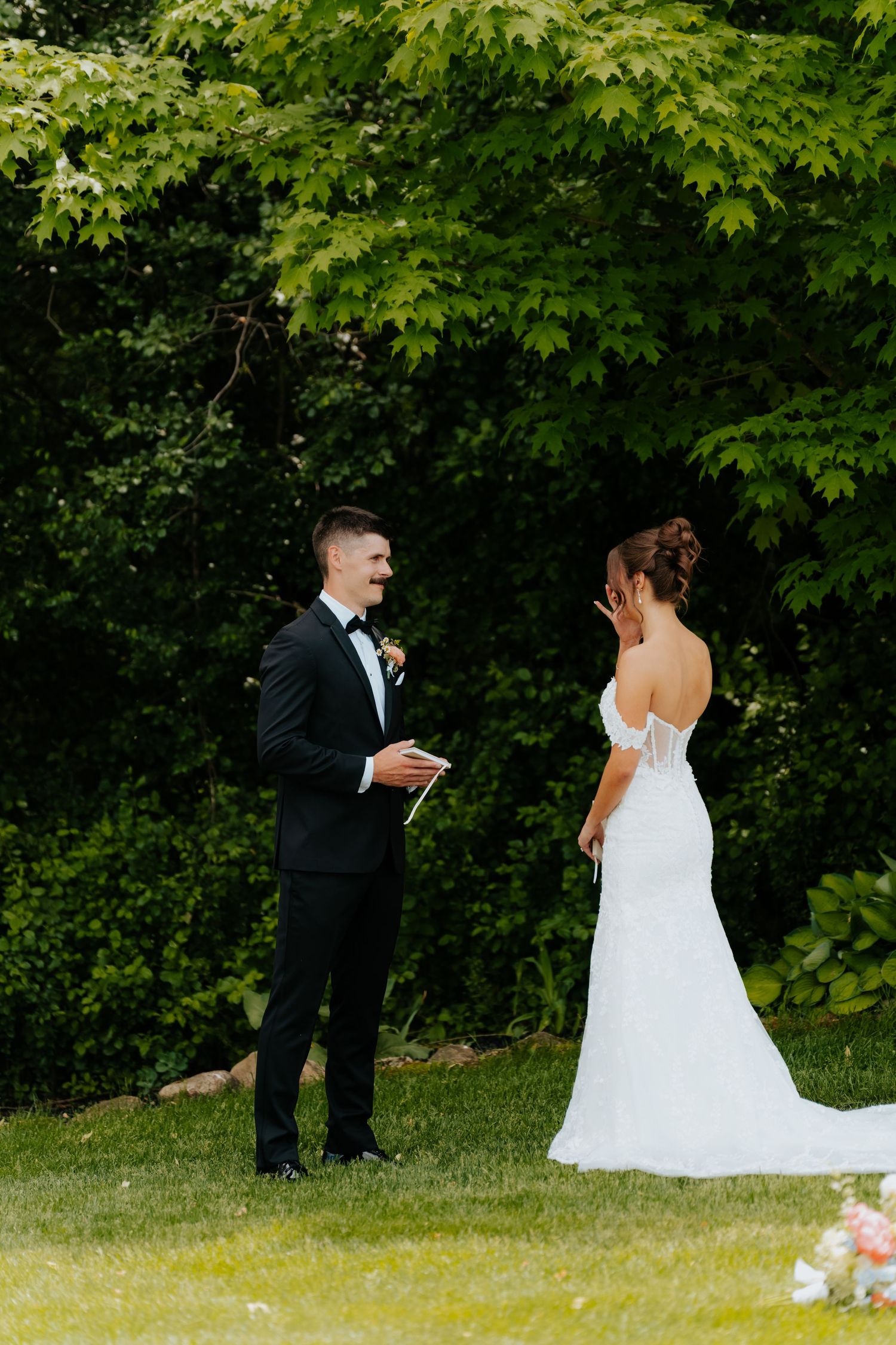 Groom reading vows to bride in white mermaid dress during outdoor wedding ceremony.