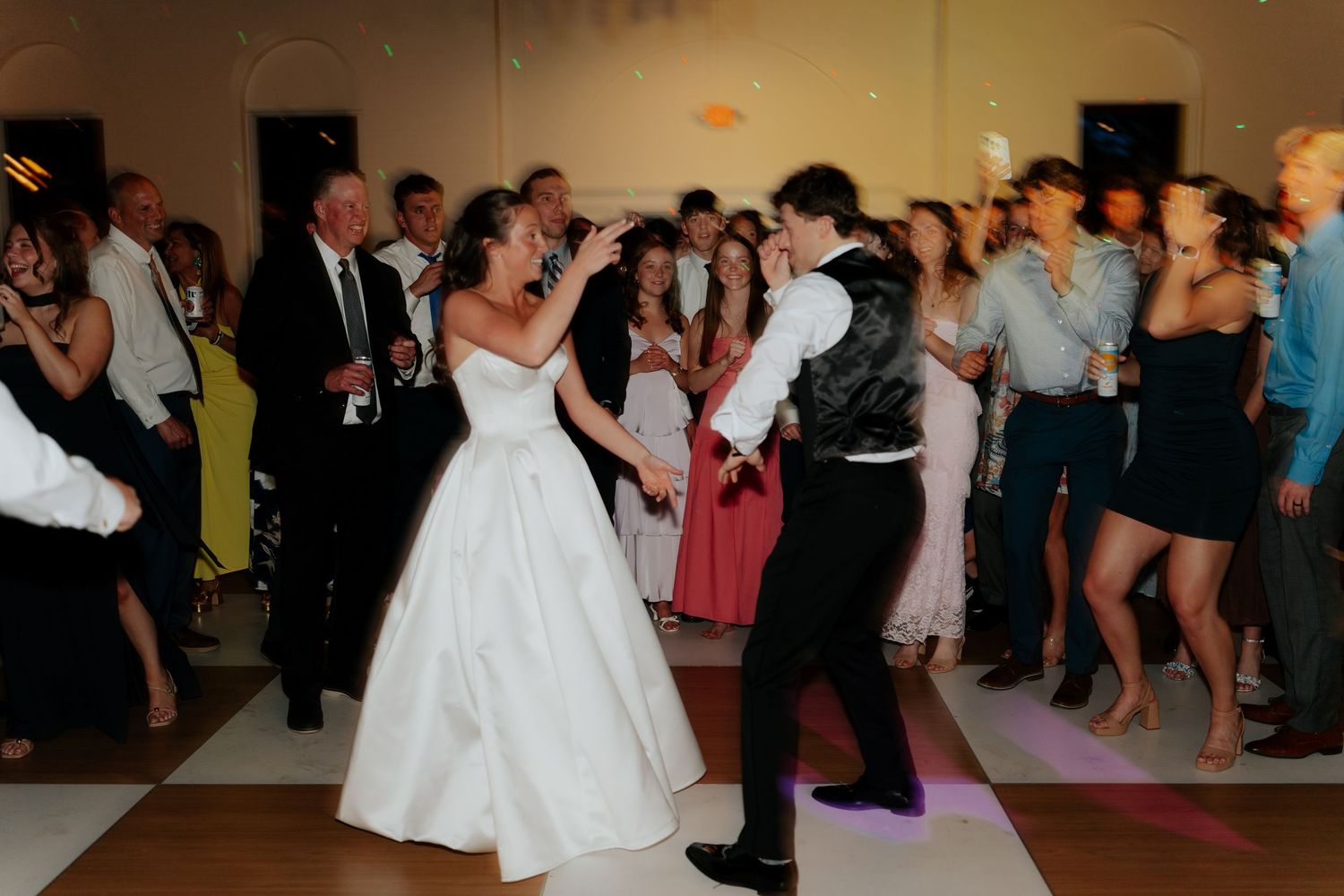 Bride and groom dancing together on wedding reception dance floor surrounded by guests celebrating.