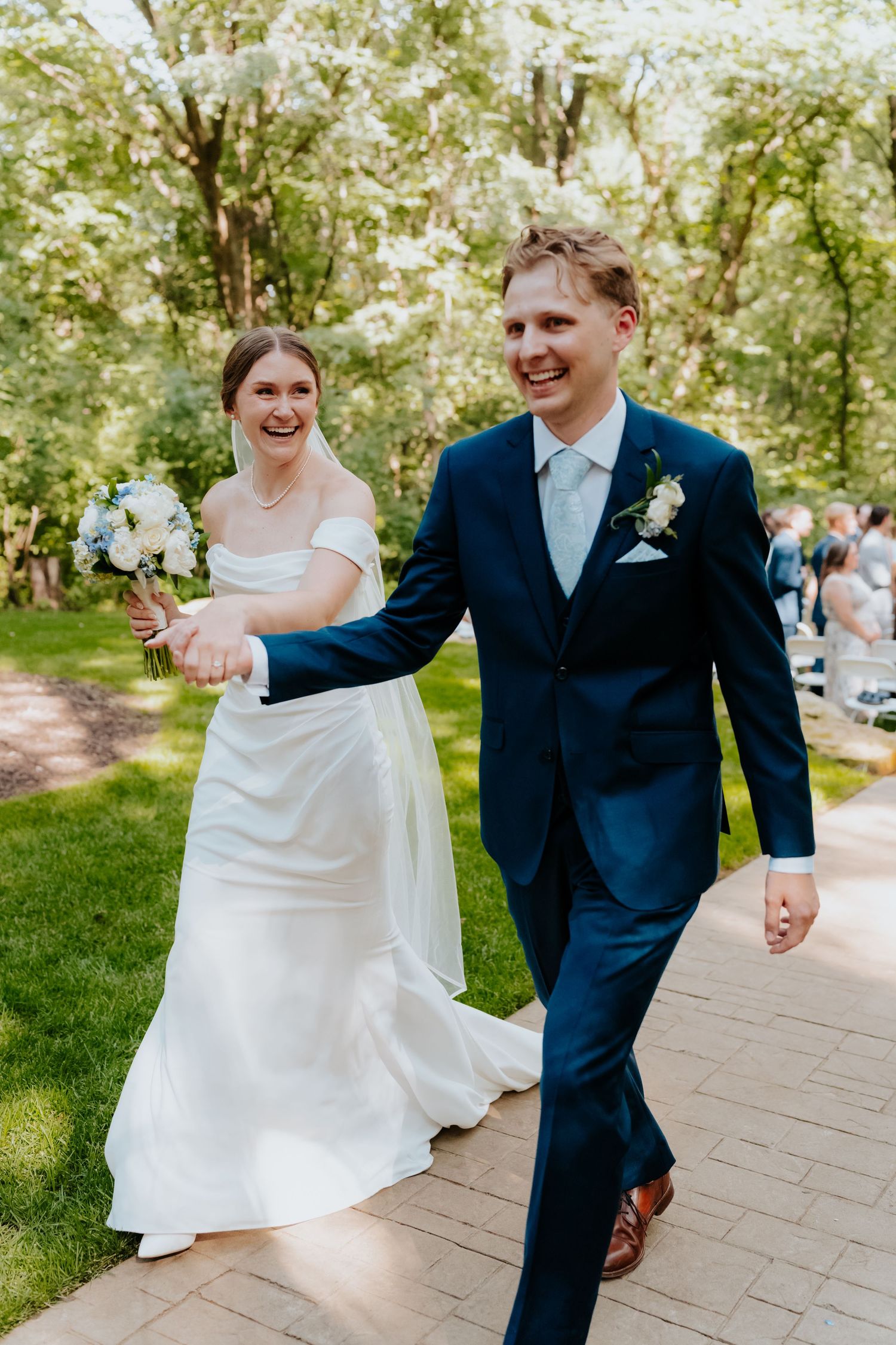 Happy bride and groom walking hand in hand on a brick path through a green park after their wedding ceremony.