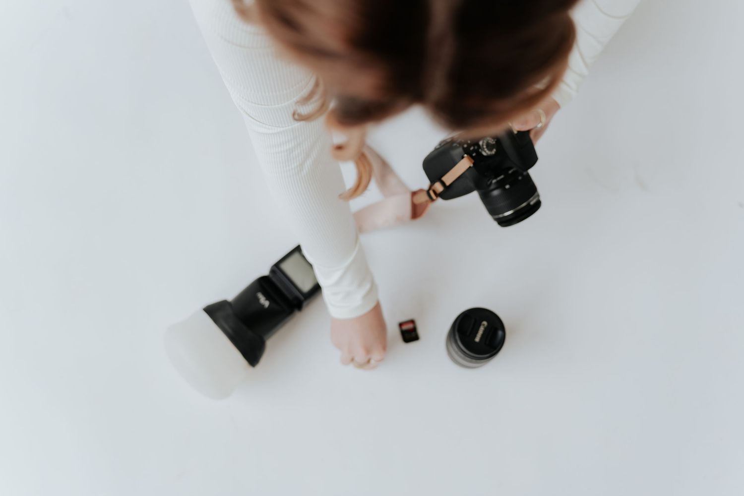 Overhead view of a female photographer holding a Canon DSLR camera with a lens and flash on a white surface.