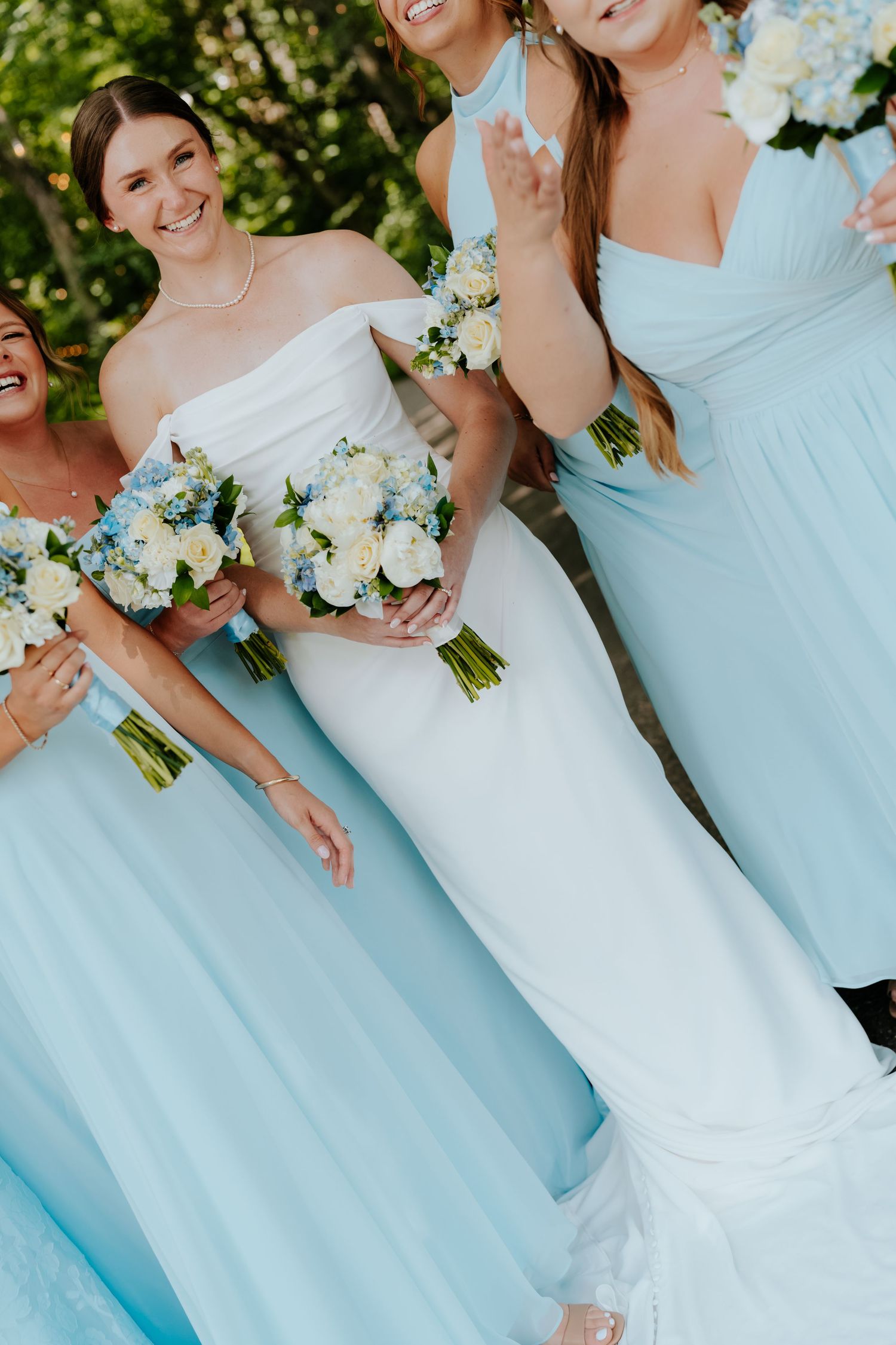 Bride in white strapless gown with bridesmaids in light blue dresses holding white and blue bouquets.