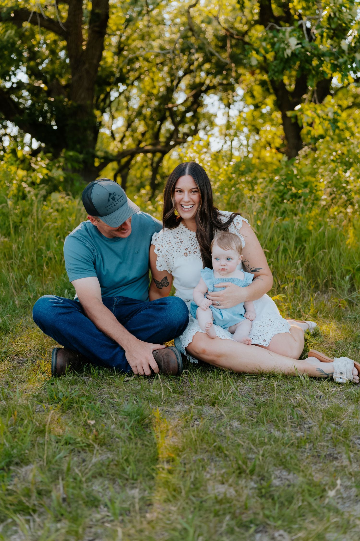 A happy family with a baby sits on grass under golden trees during an outdoor photo session.