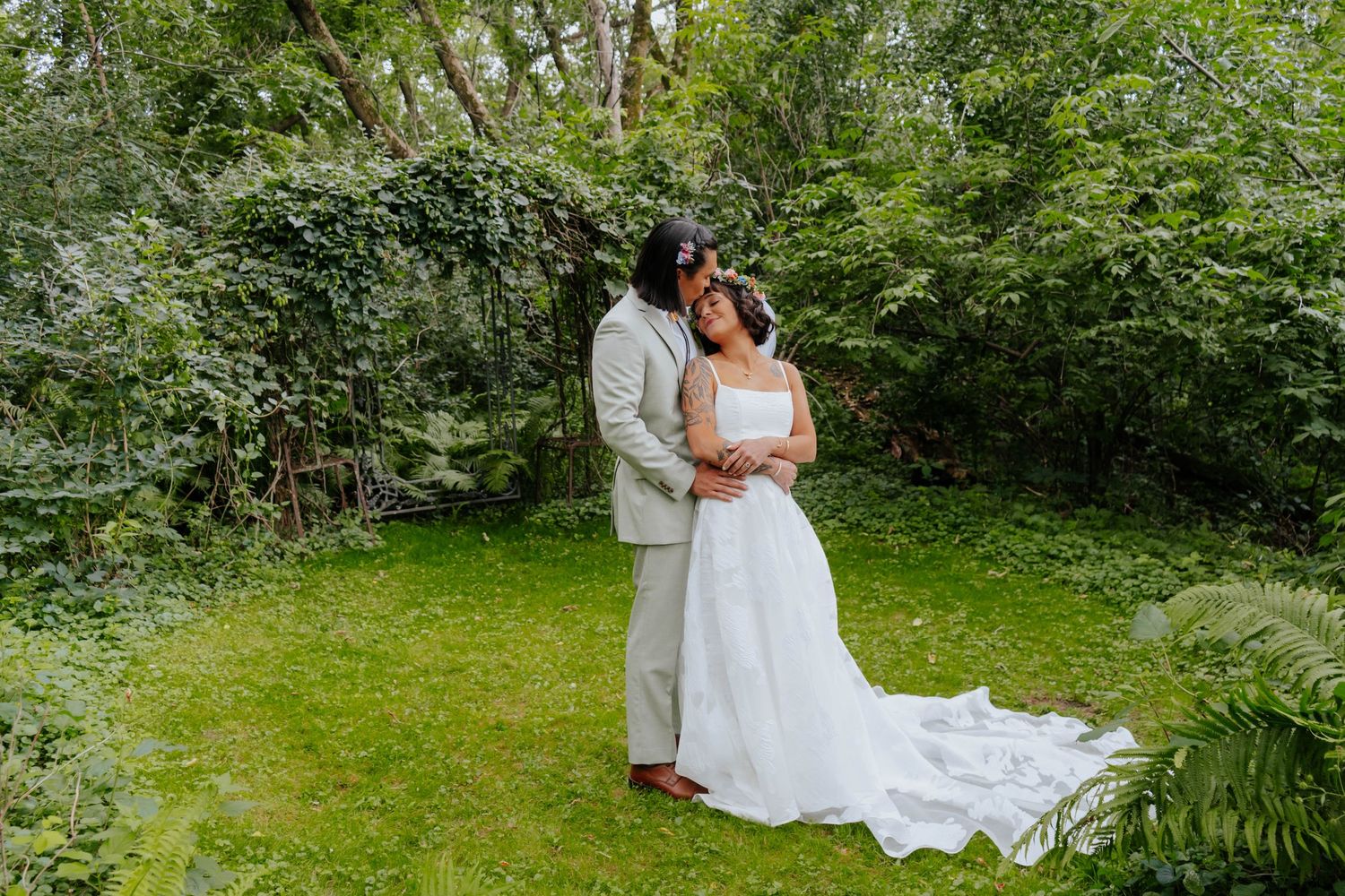 Wedding couple posing in garden setting with flowing white dress and formal attire.