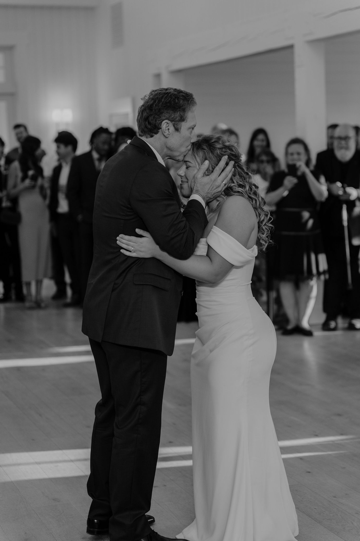 Black and white photo of a bride and groom sharing a first dance kiss at their wedding reception.