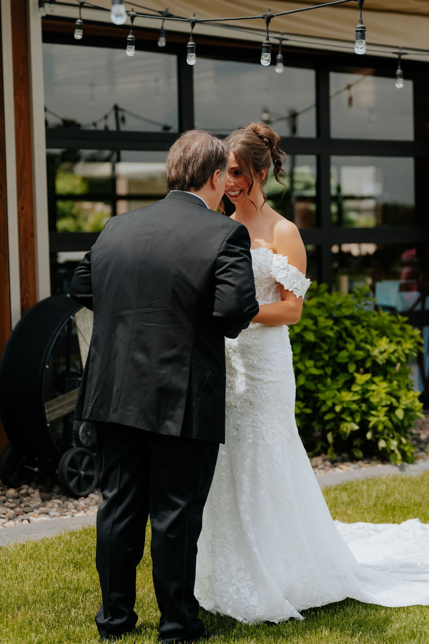 Father of the bride sharing emotional first look moment with bride in white lace gown outdoors.