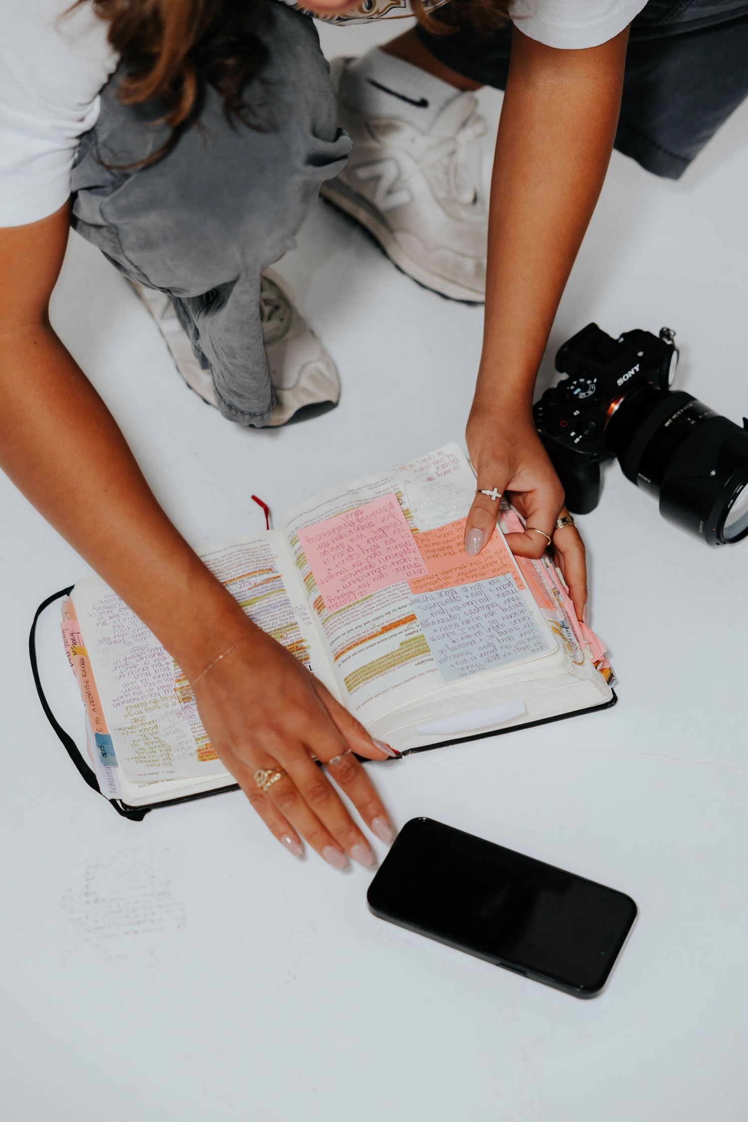 Woman reviewing a colorful annotated journal notebook beside a smartphone and camera on a white surface.